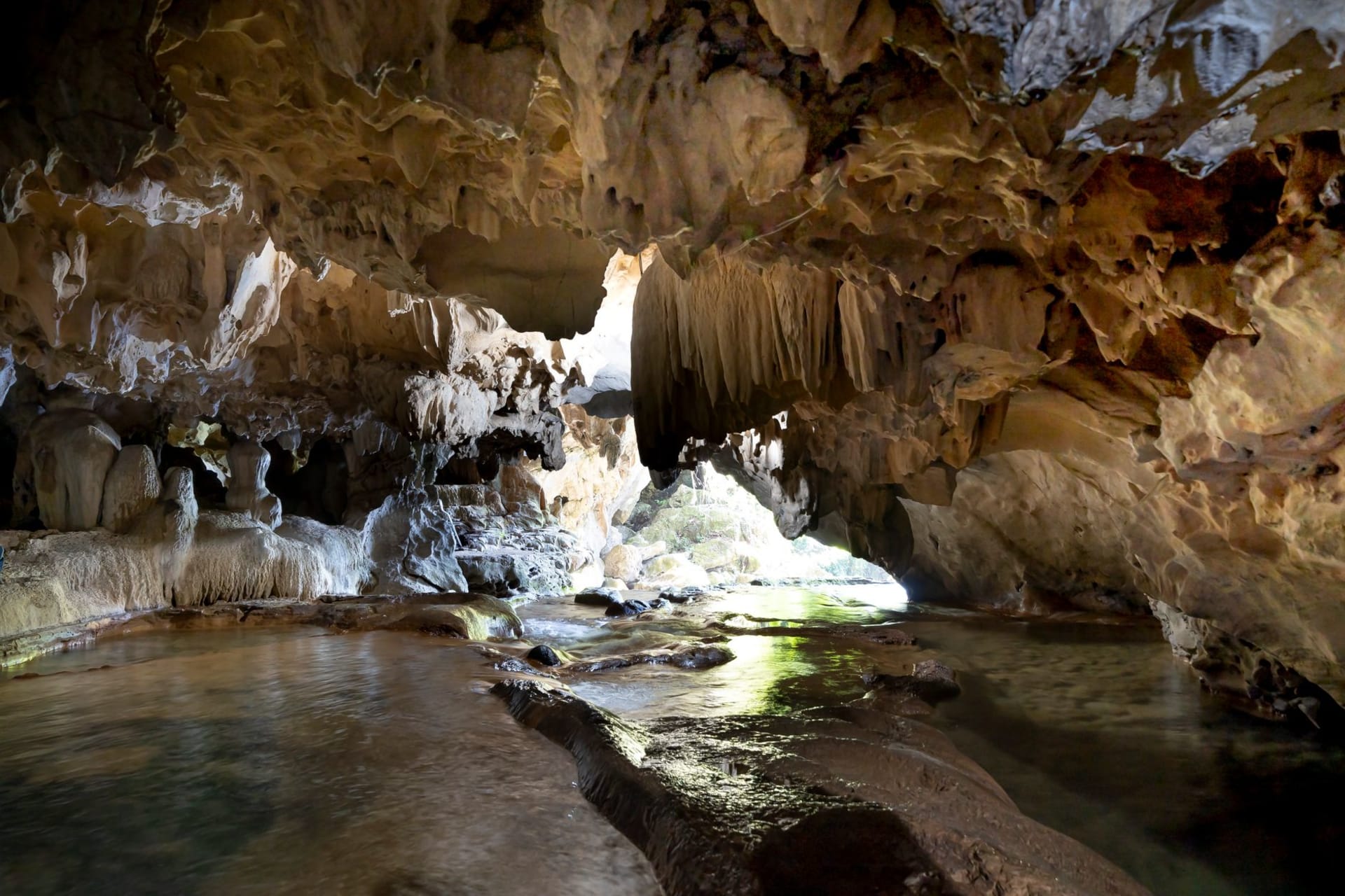 Wooden boat entering the illuminated river mouth of Phong Nha Cave with limestone karst walls rising from green water