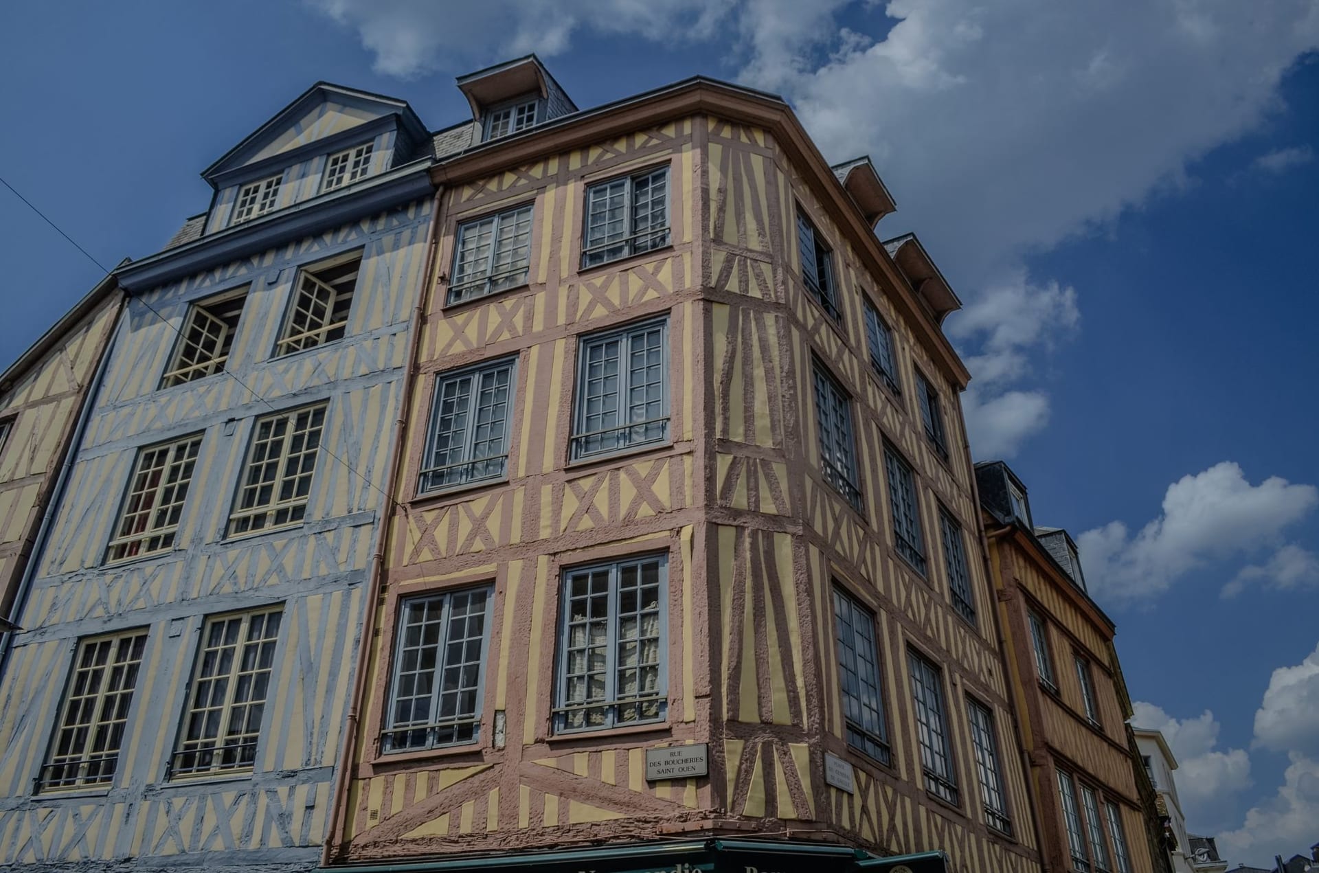 Half-timbered medieval houses leaning toward each other over a narrow cobblestone street in Troyes, the morning light falling in oblique gold strips