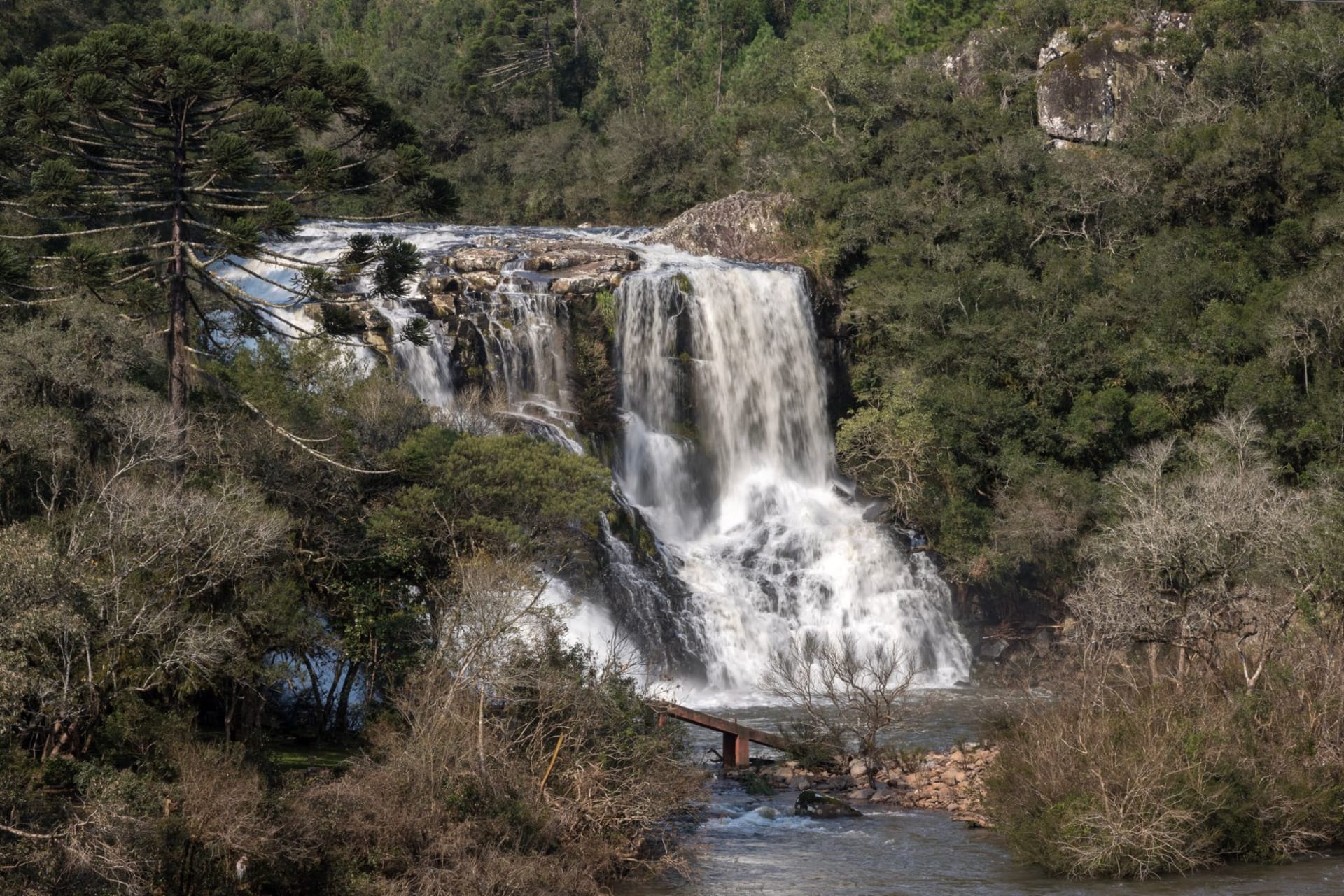 Cachoeira Santa Bárbara in full flow, multiple tiers of white water cascading over red quartzite into a wide turquoise pool framed by cerrado forest