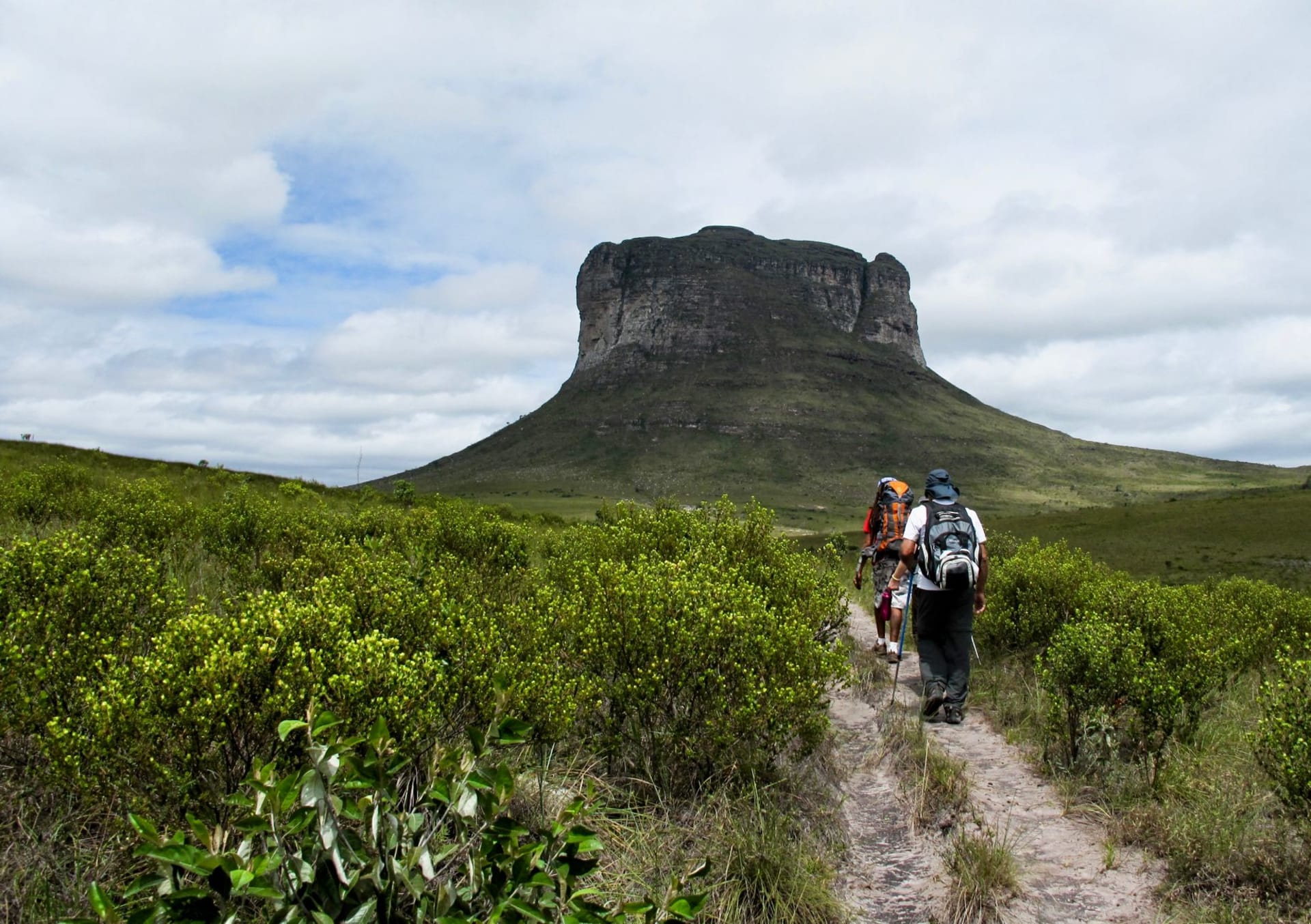 A tall waterfall dropping off a reddish cliff into a deep green canyon pool within the Chapada dos Veadeiros