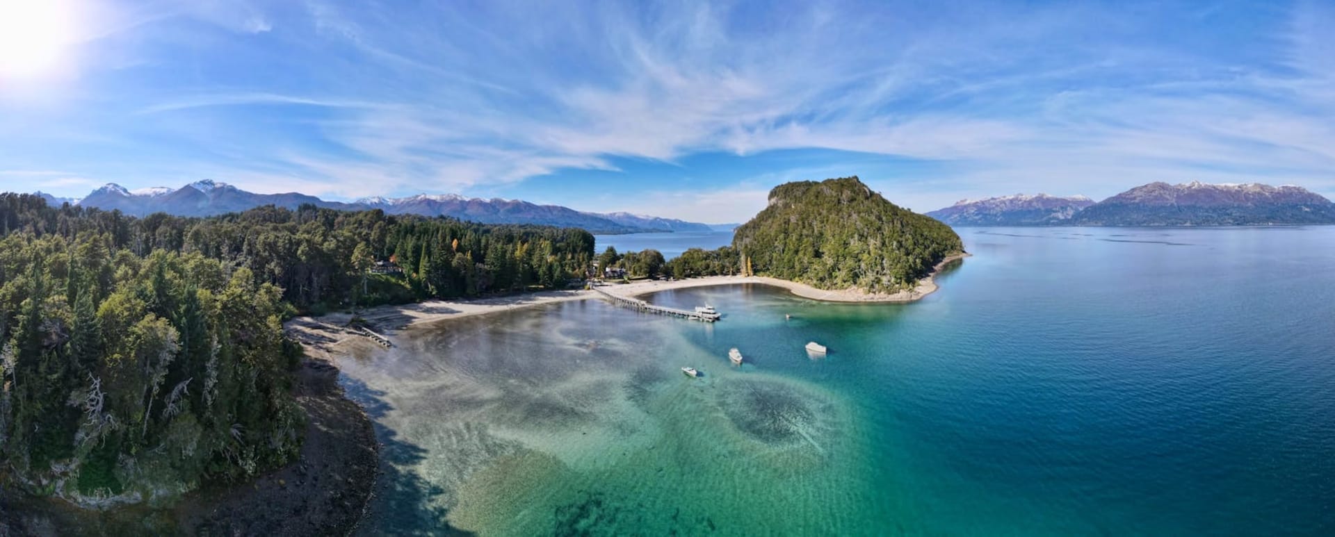 Jagged granite spires of the Dientes de Navarino rise above a valley of lenga beech trees turning autumn red, with the steel-grey waters of the Beagle Channel visible in the distance below a sky heavy with cloud.