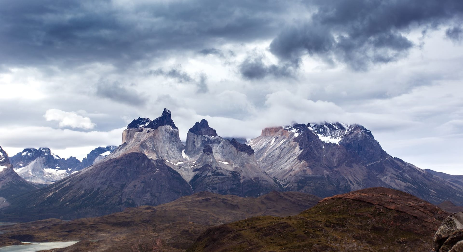 Dramáticos picos de los Andes en Torres del Paine, Chile, bajo un cielo tormentoso con naturaleza intacta en primer plano