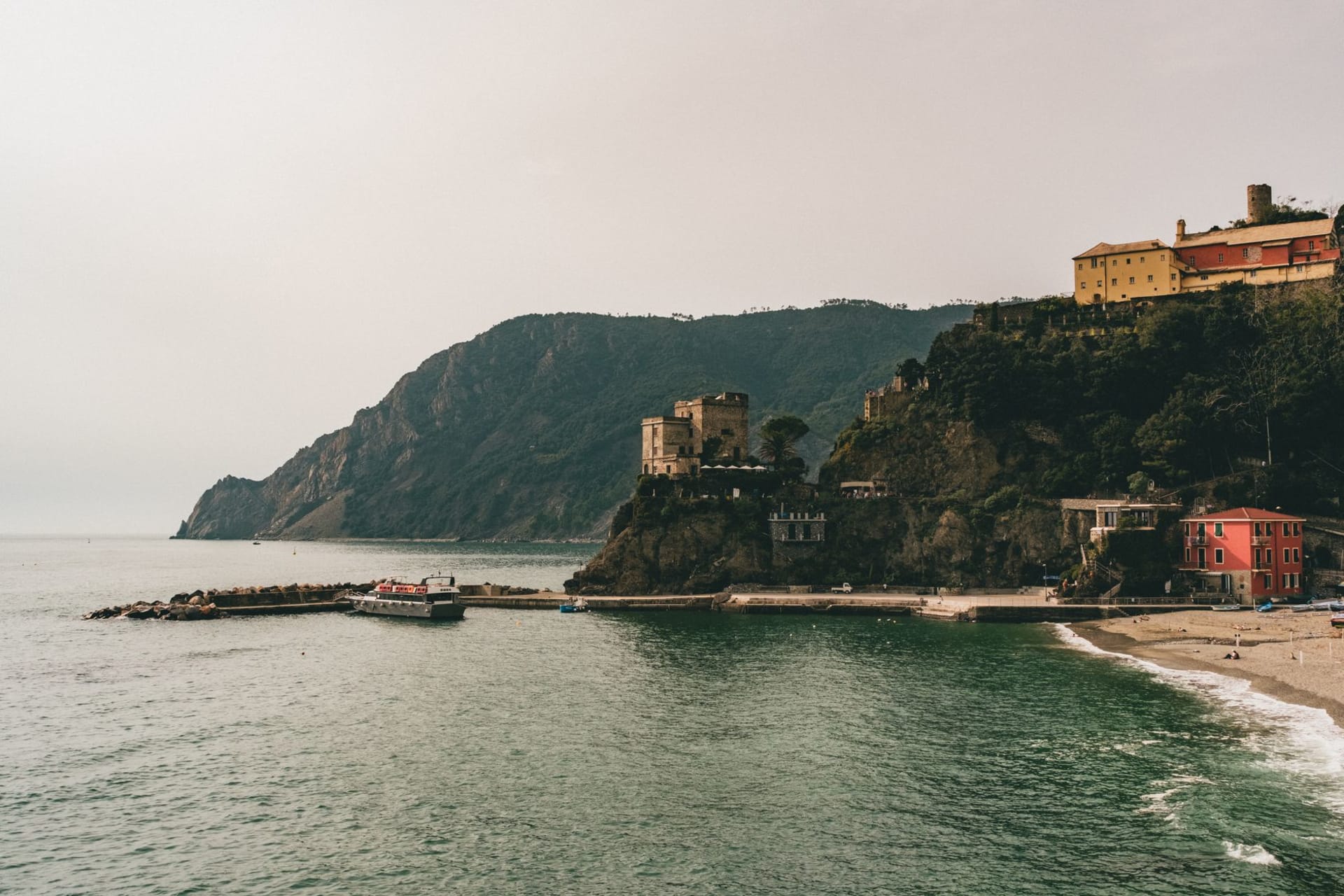 Monterosso al Mare's wide sandy beach with striped umbrellas, backed by lemon-yellow buildings and rocky headlands