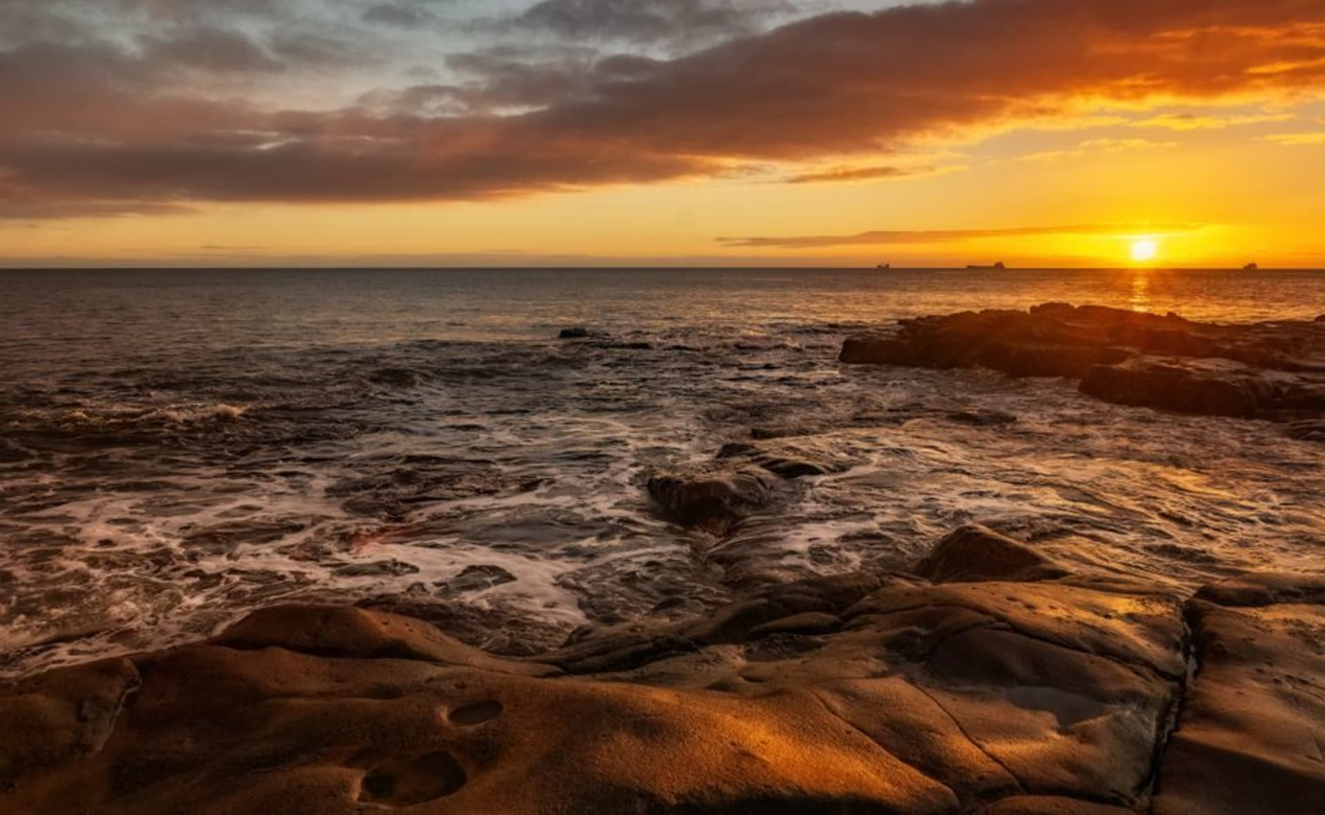 Dark volcanic rock outcrop at Black Rock on Rarotonga's coast with waves breaking against it at sunset