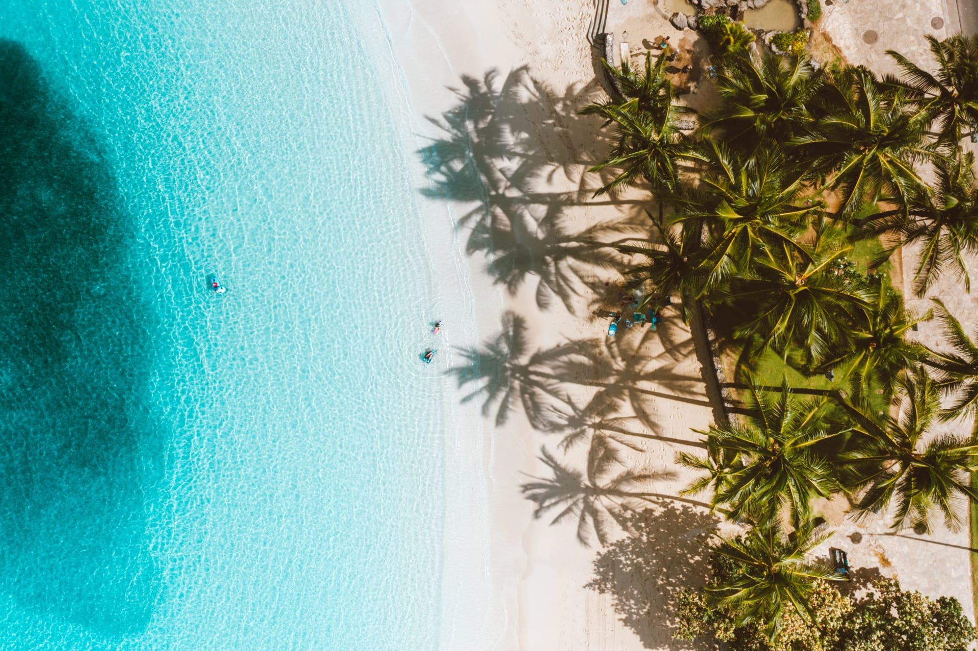 One Foot Island motu in Aitutaki Lagoon — a tiny coral sandbar edged with palms surrounded by vivid turquoise water