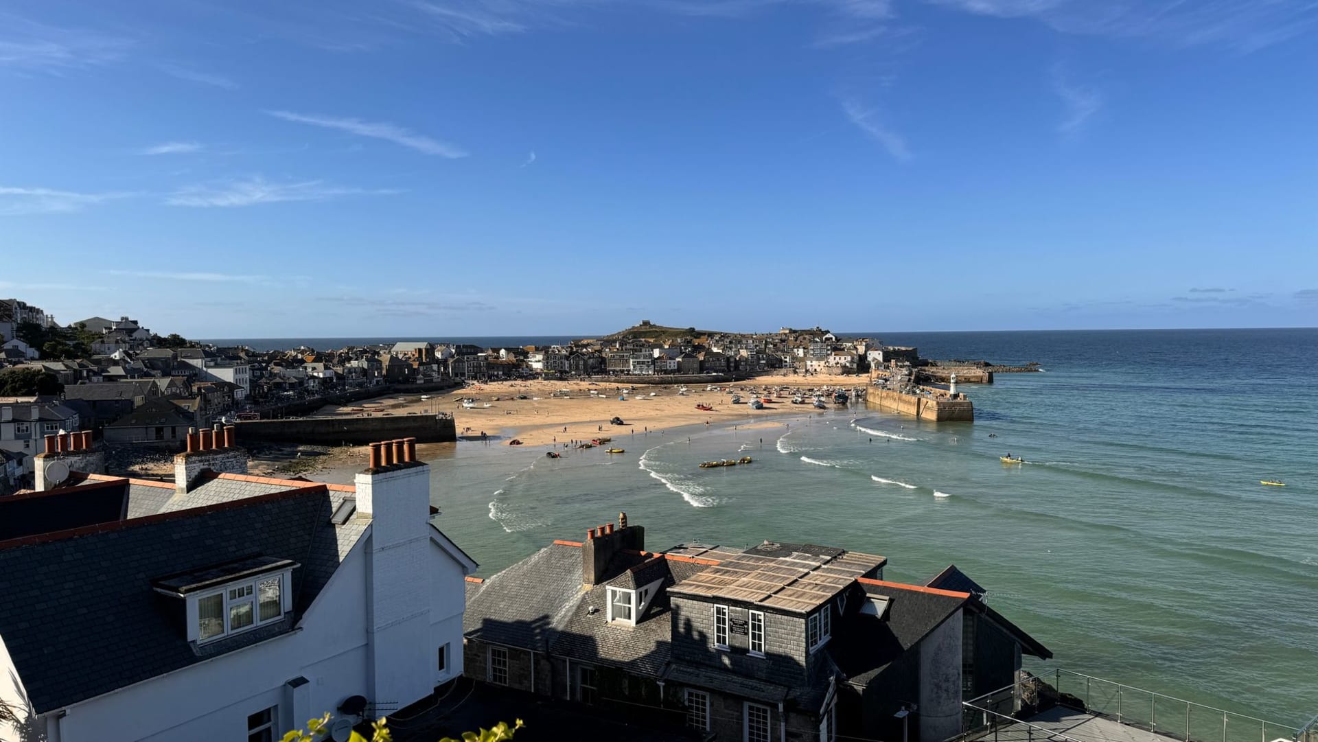 St Ives beach and harbor with whitewashed coastal townhouses stacked up the hillside under soft light