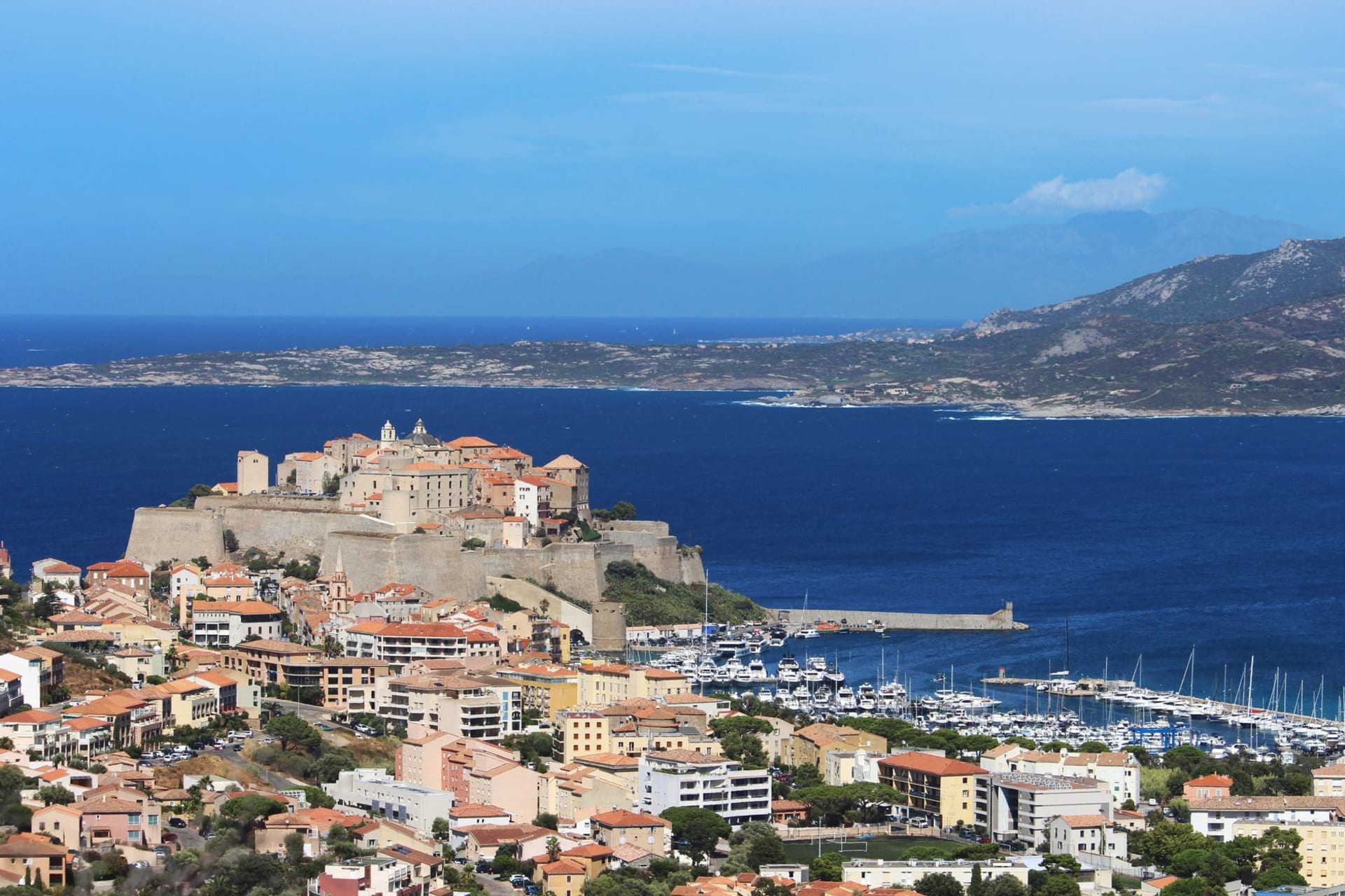 Calvi's Genoese citadel on its headland above the turquoise bay, snow-capped Monte Cinto visible in the distance