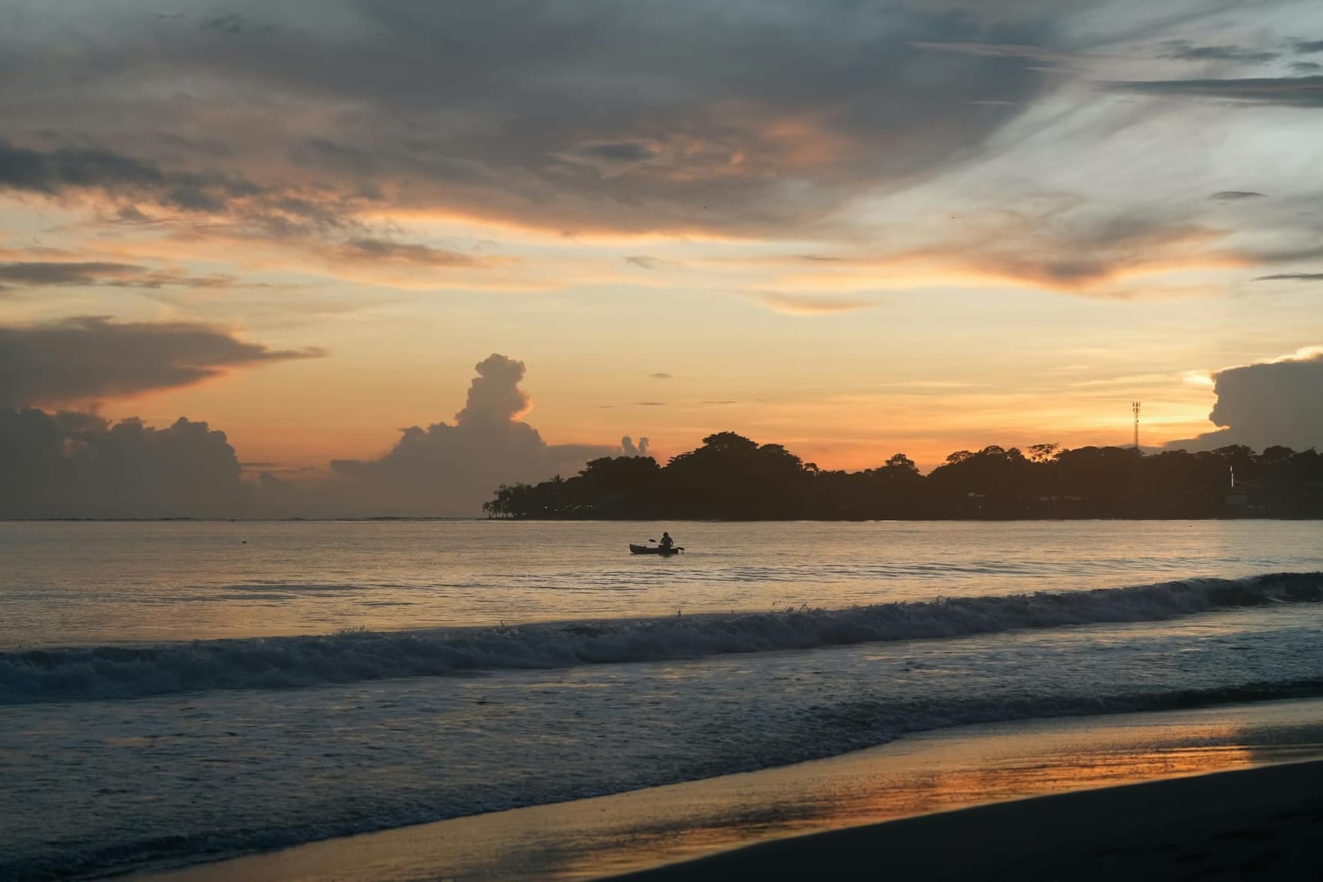 A palm-fringed Caribbean beach at golden hour, shallow turquoise water meeting coral-sand shore, dense jungle pressing to the waterline