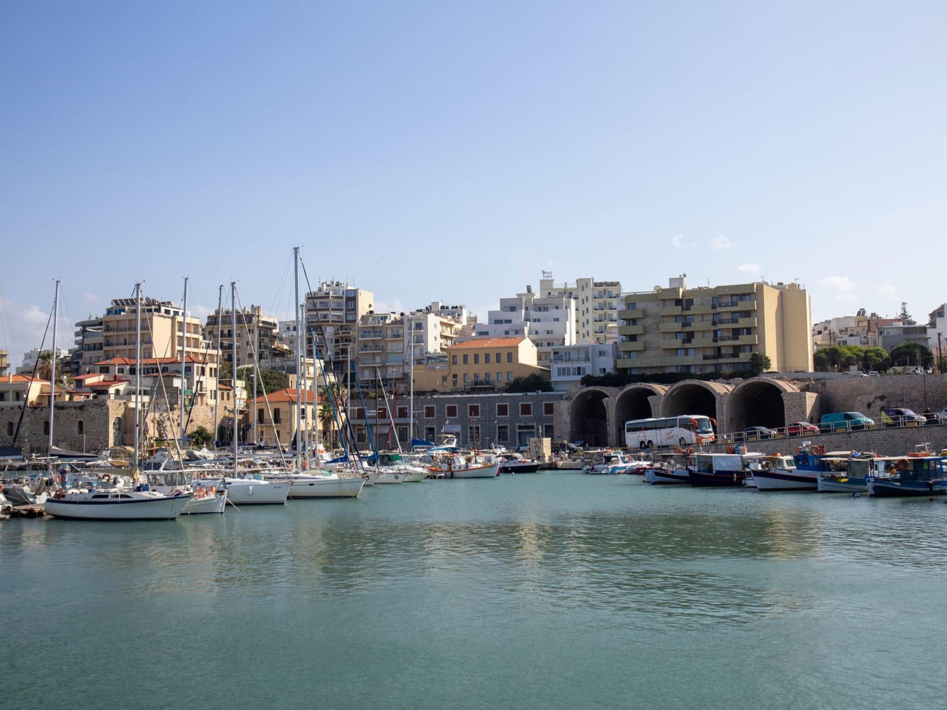 The Koules Venetian sea fortress at Heraklion harbor glowing amber in late afternoon light, with fishing boats moored below