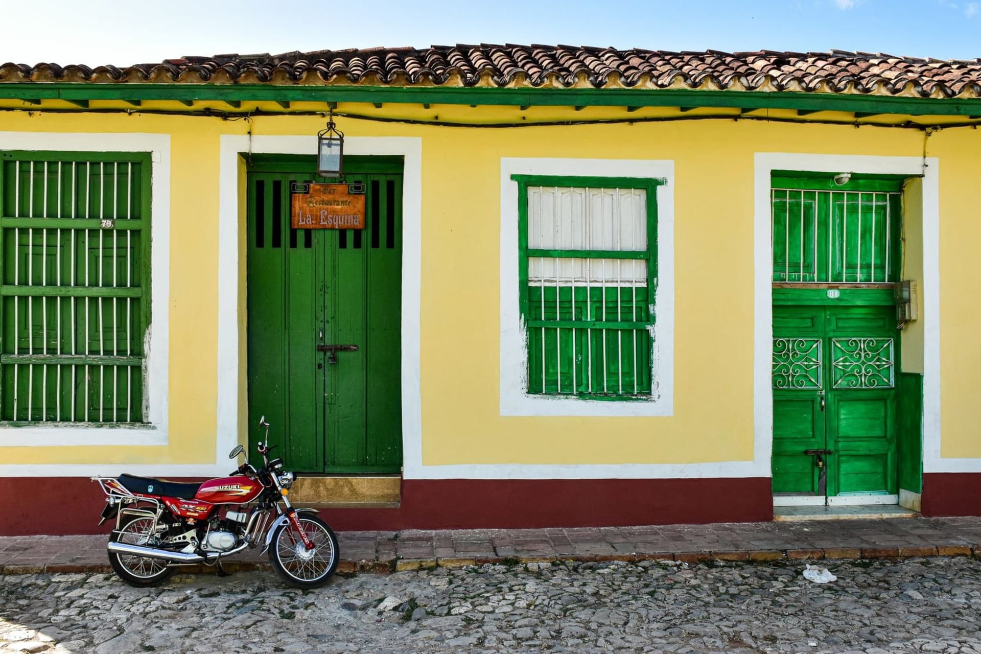 A cobblestone street in Trinidad Cuba lined with pastel colonial houses in ochre, turquoise, and terracotta under a bright Caribbean sky