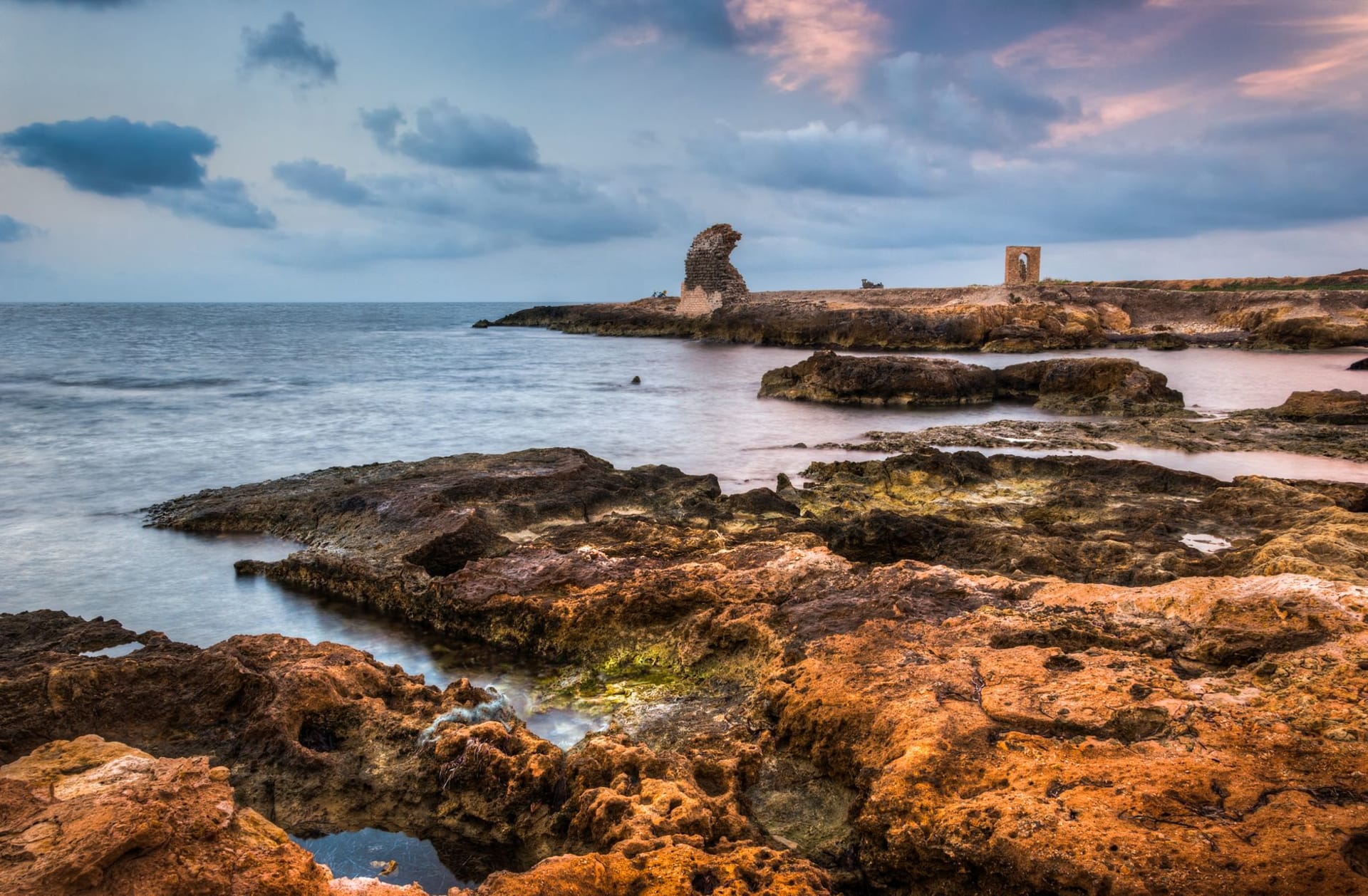 Rocky coastline with ancient ruins at sunset, waves breaking against weathered stone