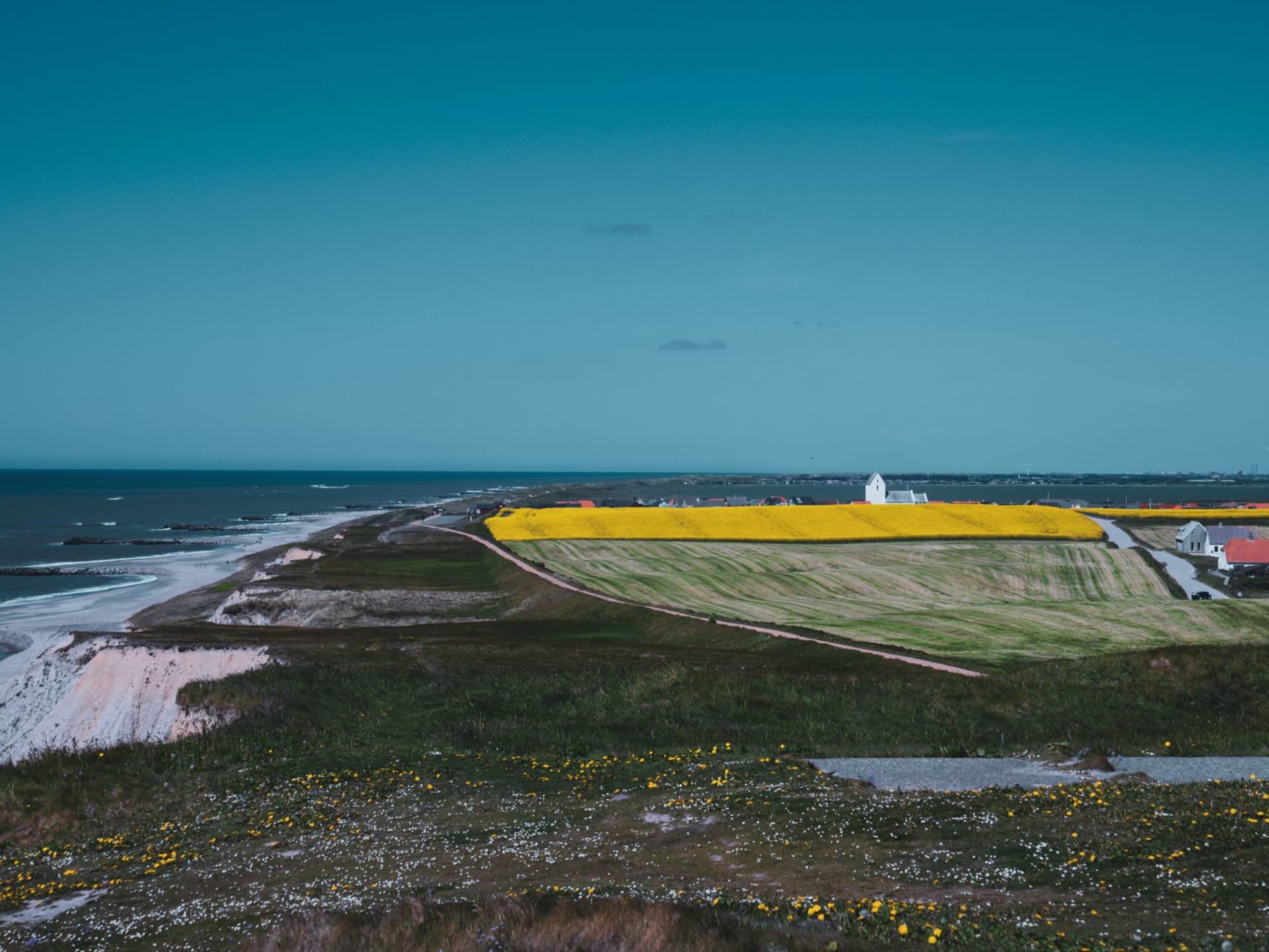 Les tours caractéristiques roses et blanches du château de Tranekær s'élevant au-dessus de la forêt de hêtres sur Langeland, avec les eaux calmes du Petit Belt visible en arrière-plan