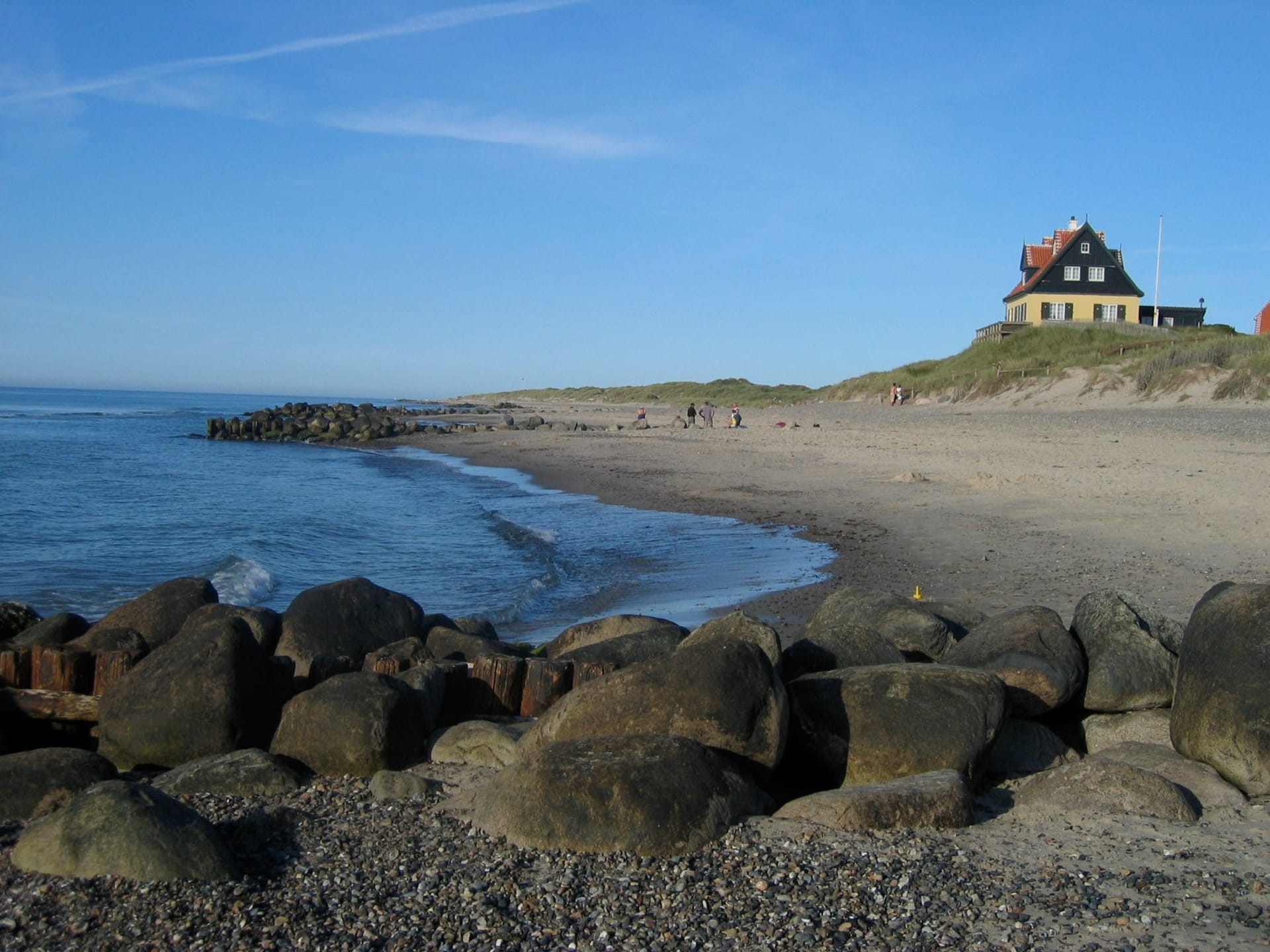 Rolling green farmland on Samsø with offshore wind turbines visible on the horizon and a bright blue Kattegat sky above, the island's characteristic flat agricultural landscape stretching to the sea