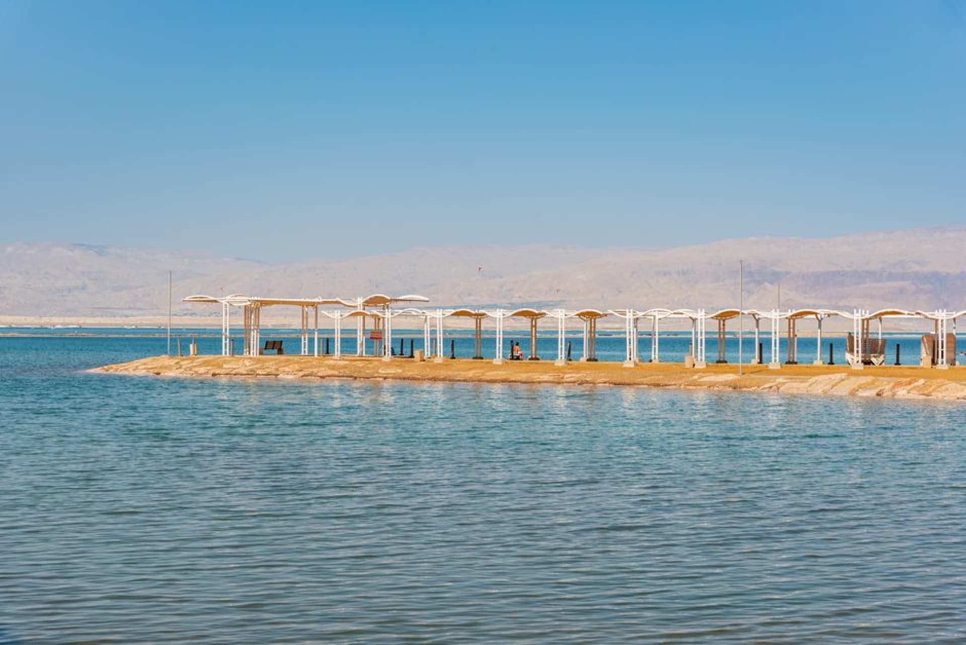 Un alignement d'hôtels-spas le long du rivage d'Ein Bokek à la mer Morte, transats alignés sur la plage et eau bleue et calme au-delà