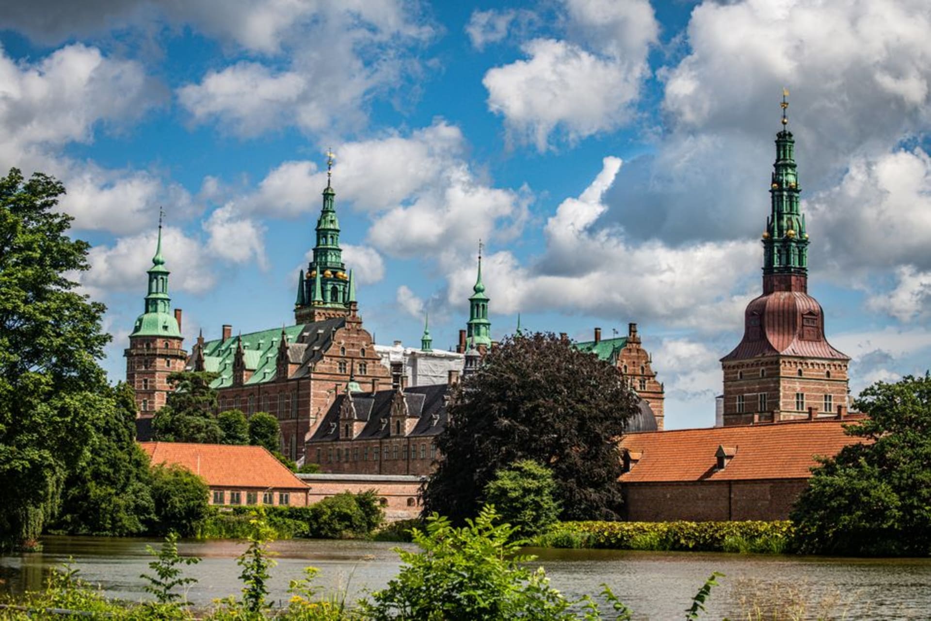 Red-brick Renaissance castle with green copper spires reflected in the surrounding lake
