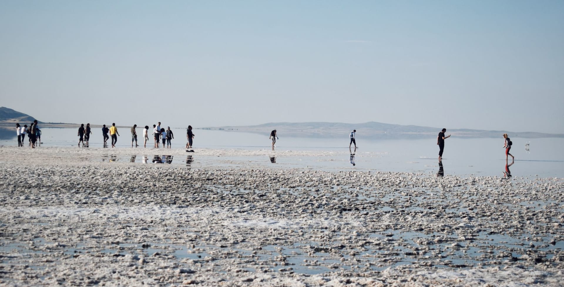 Travelers walking along the glassy white shore of Lake Assal, the salt crust reflecting a deep blue sky