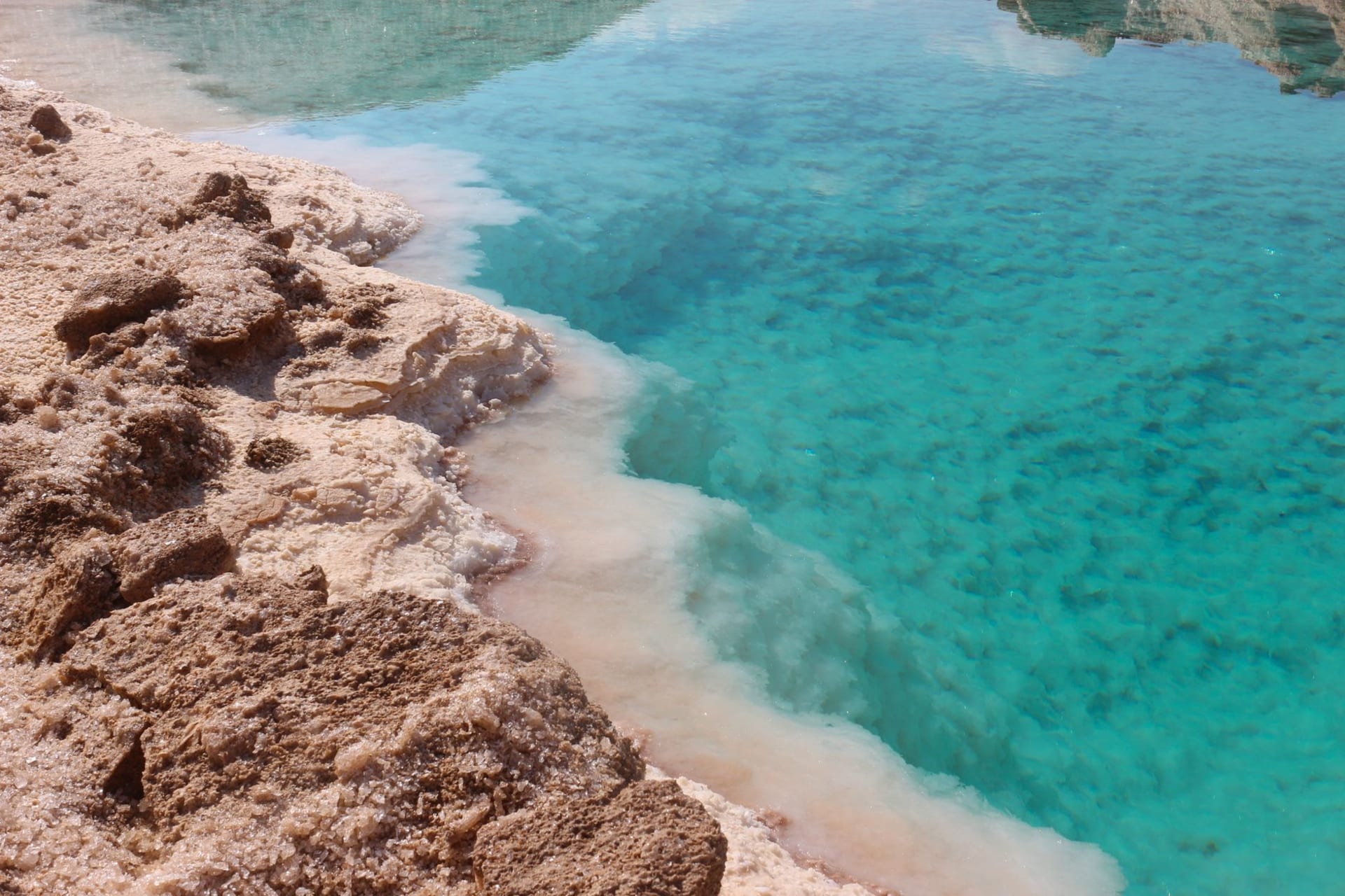 The blinding white salt crust of Lake Assal stretching to chemical-blue water under a cloudless sky