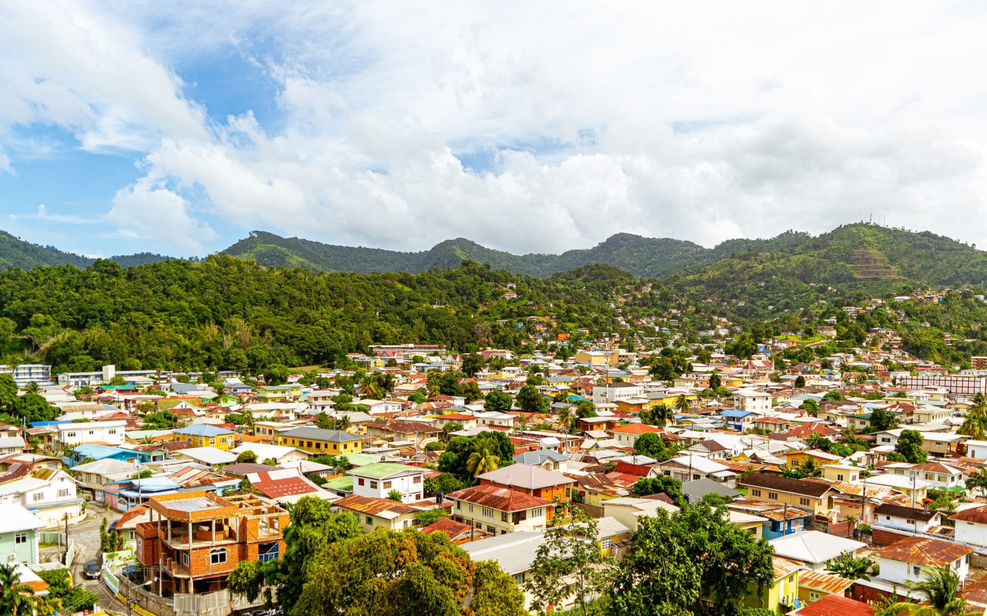 Colourful wooden colonial buildings along a narrow Roseau street with green hills rising behind