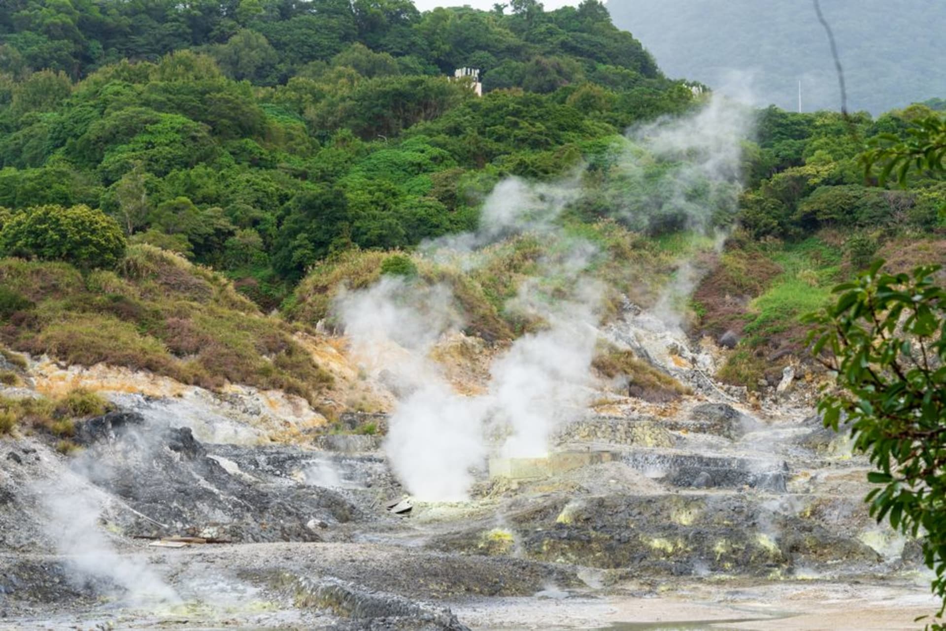 Poza termal de azufre humeante construida con roca volcánica en Wotten Waven, rodeada de plantas tropicales