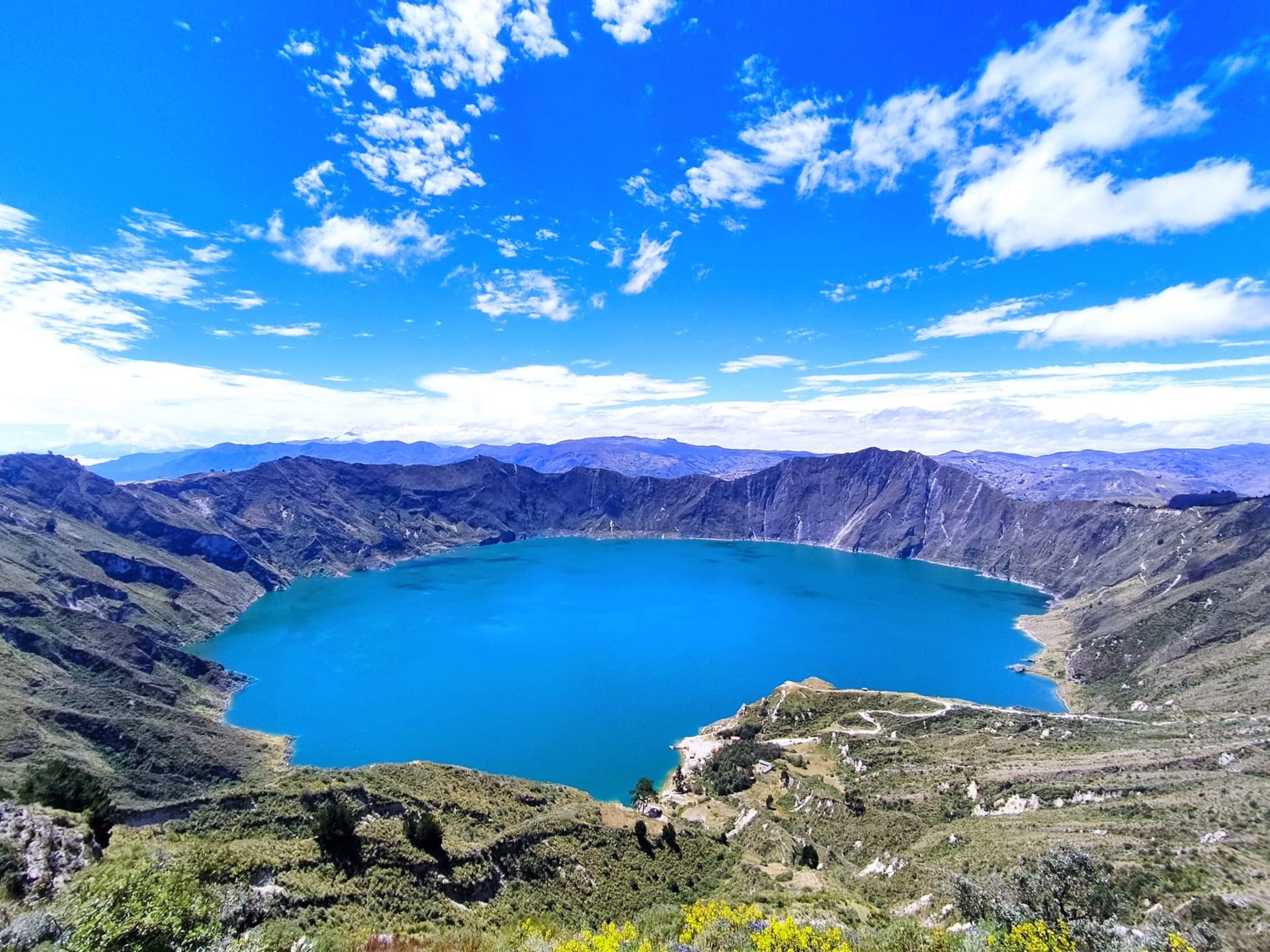 Quilotoa crater lake glowing turquoise-green inside the caldera rim under a wide Andean sky