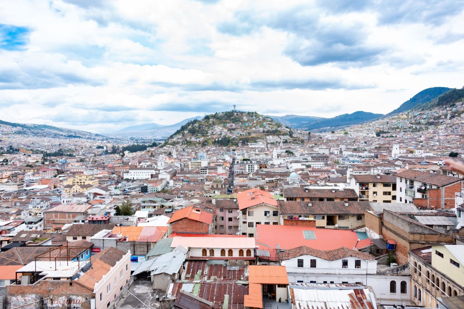 Baroque colonial church facades rising above red-tiled rooftops in Quito's historic center, with Pichincha volcano looming white-capped in the background under a deep blue Andean sky