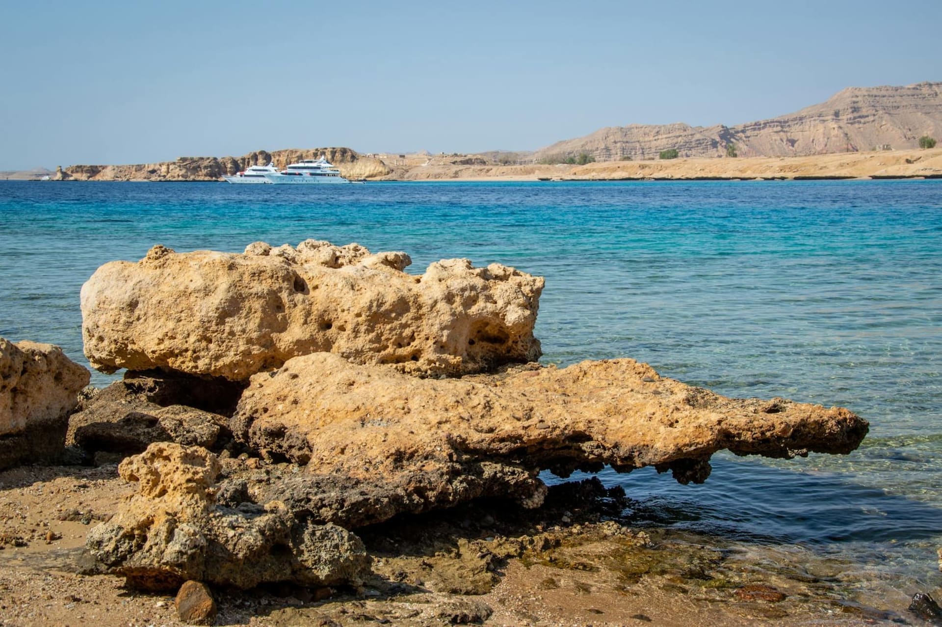 Aerial view of Ras Mohammed's limestone headland where the turquoise Red Sea and deeper blue Gulf of Aqaba converge, with coral reefs visible beneath the surface and white sand banks catching the midday light.
