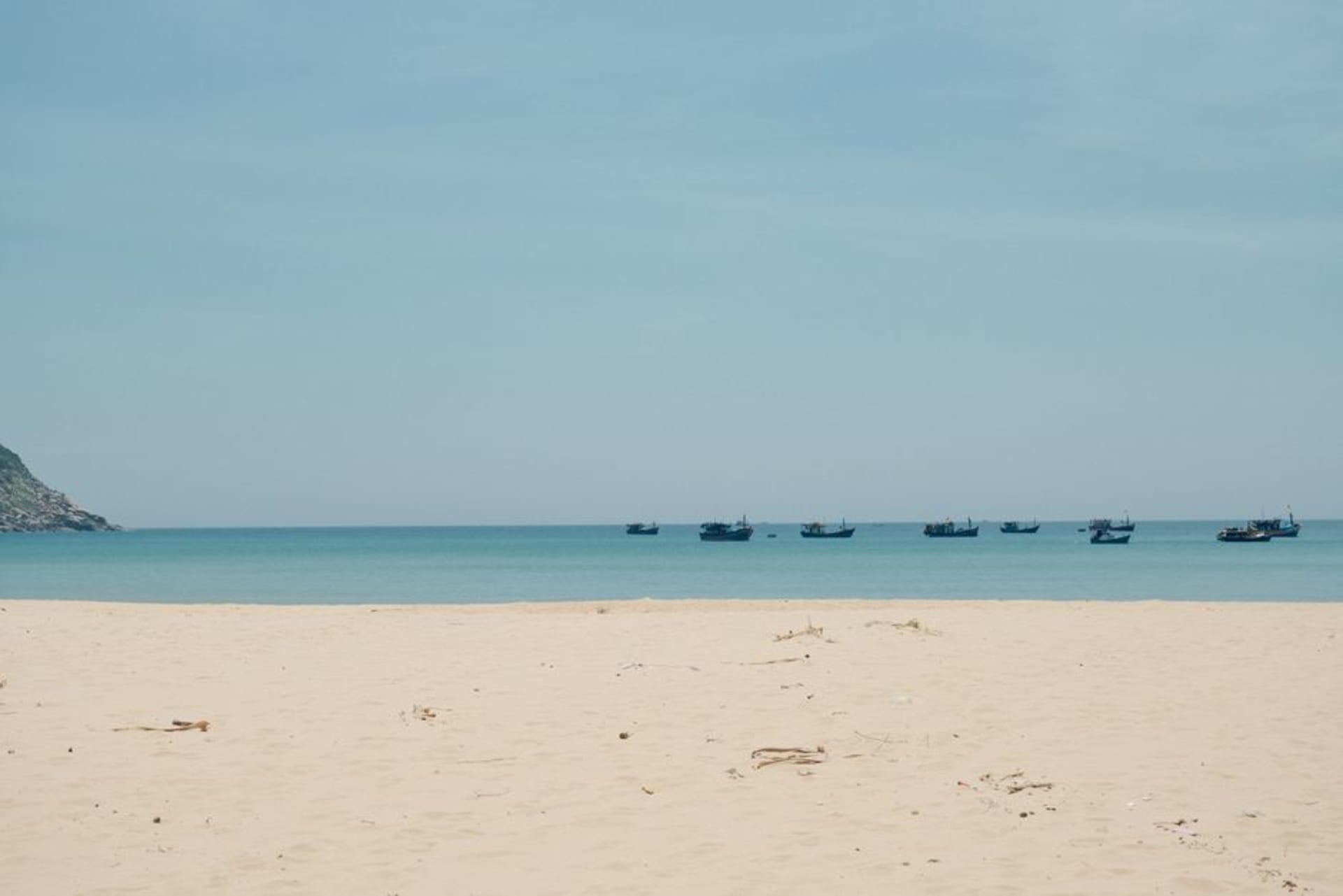 Une large étendue de plage presque déserte à El Cuco, avec des bateaux de pêche reposant sur le sable sous un ciel brumeux d'après-midi