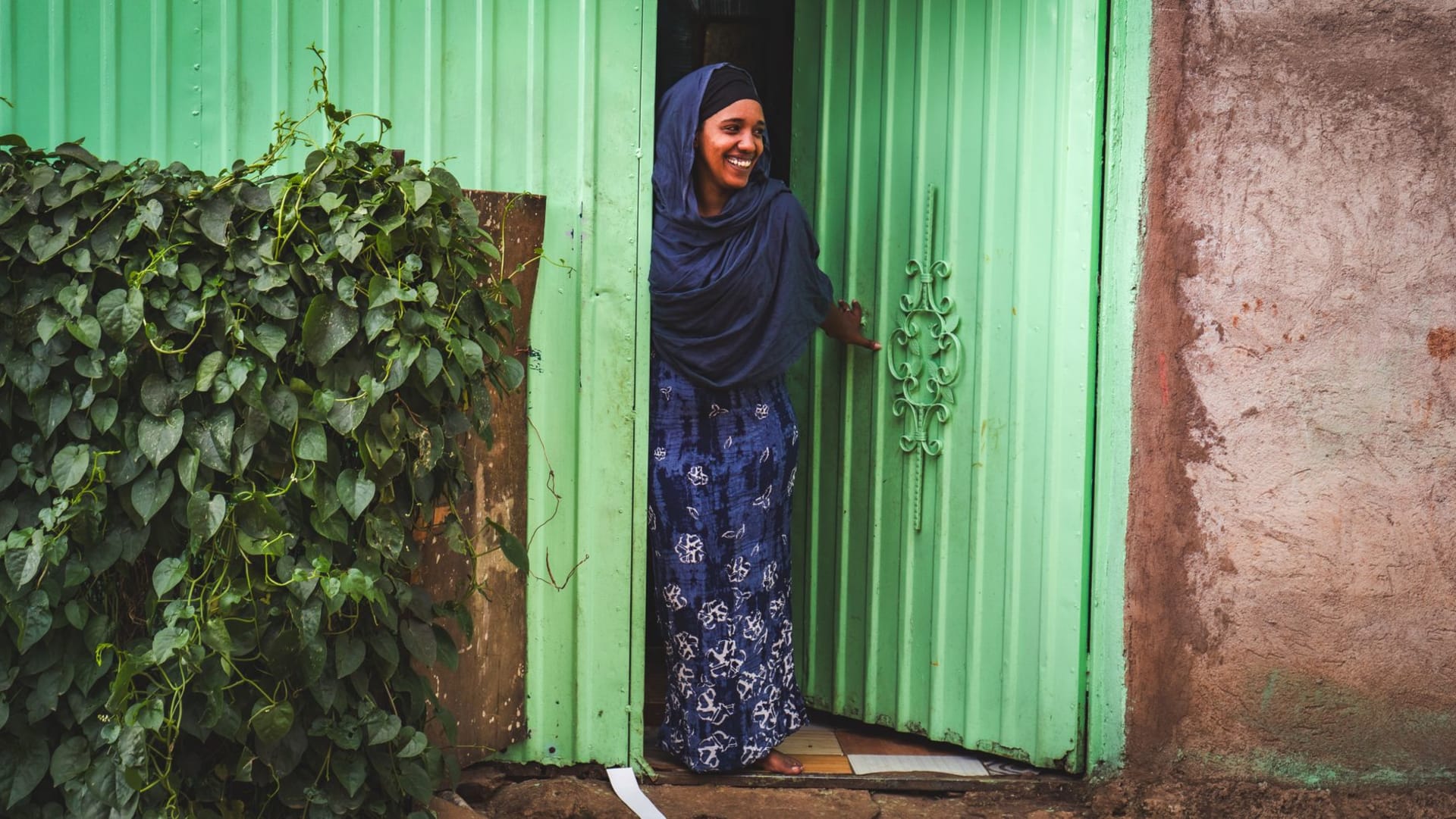 A narrow lane in Harar Jugol at dusk, whitewashed walls glowing orange under a single lamp, a woman in a bright shawl passing through