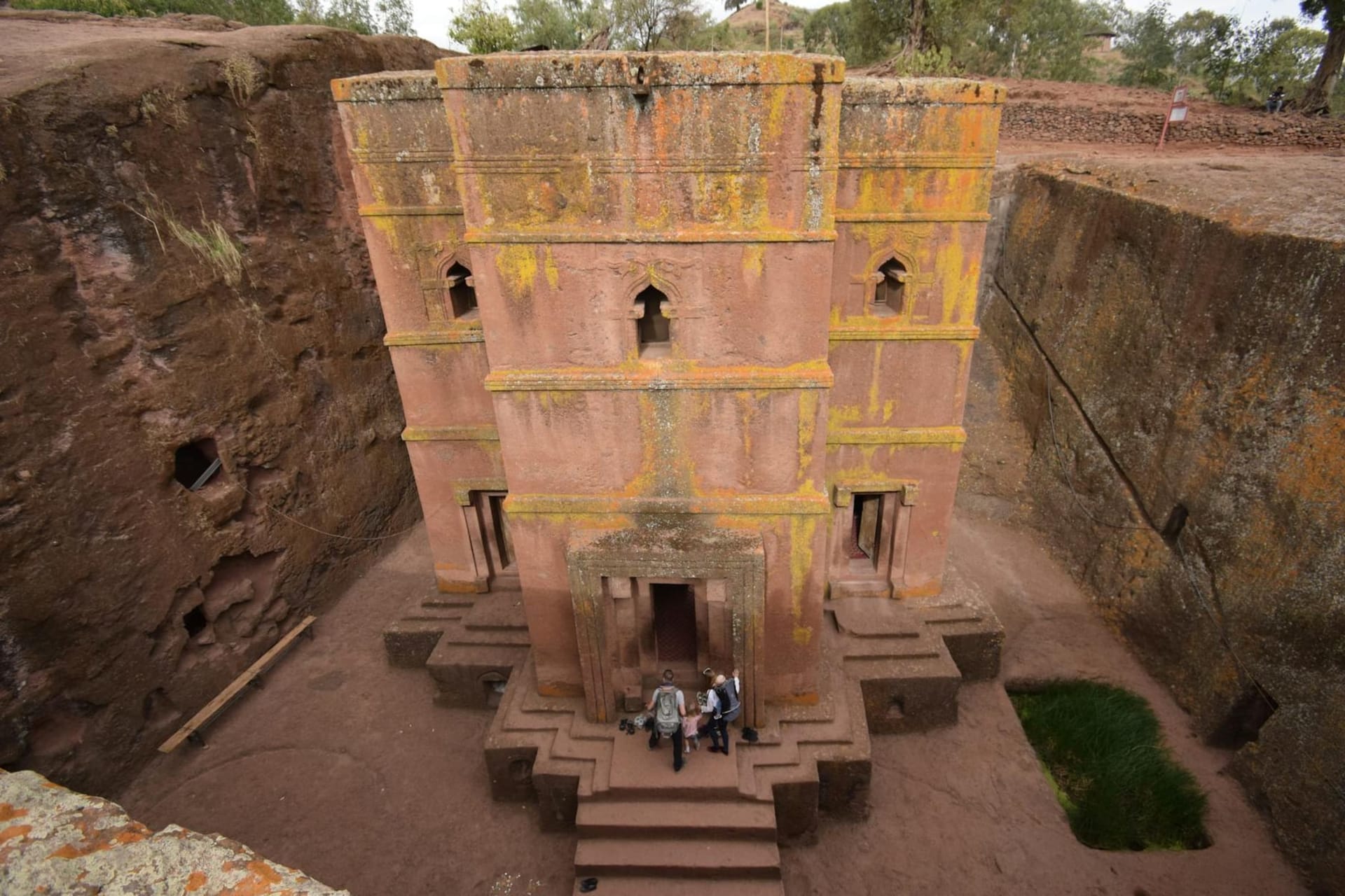 Orthodox pilgrims in white cotton robes descend into a rock-hewn church carved deep into red volcanic stone, Lalibela, Ethiopia