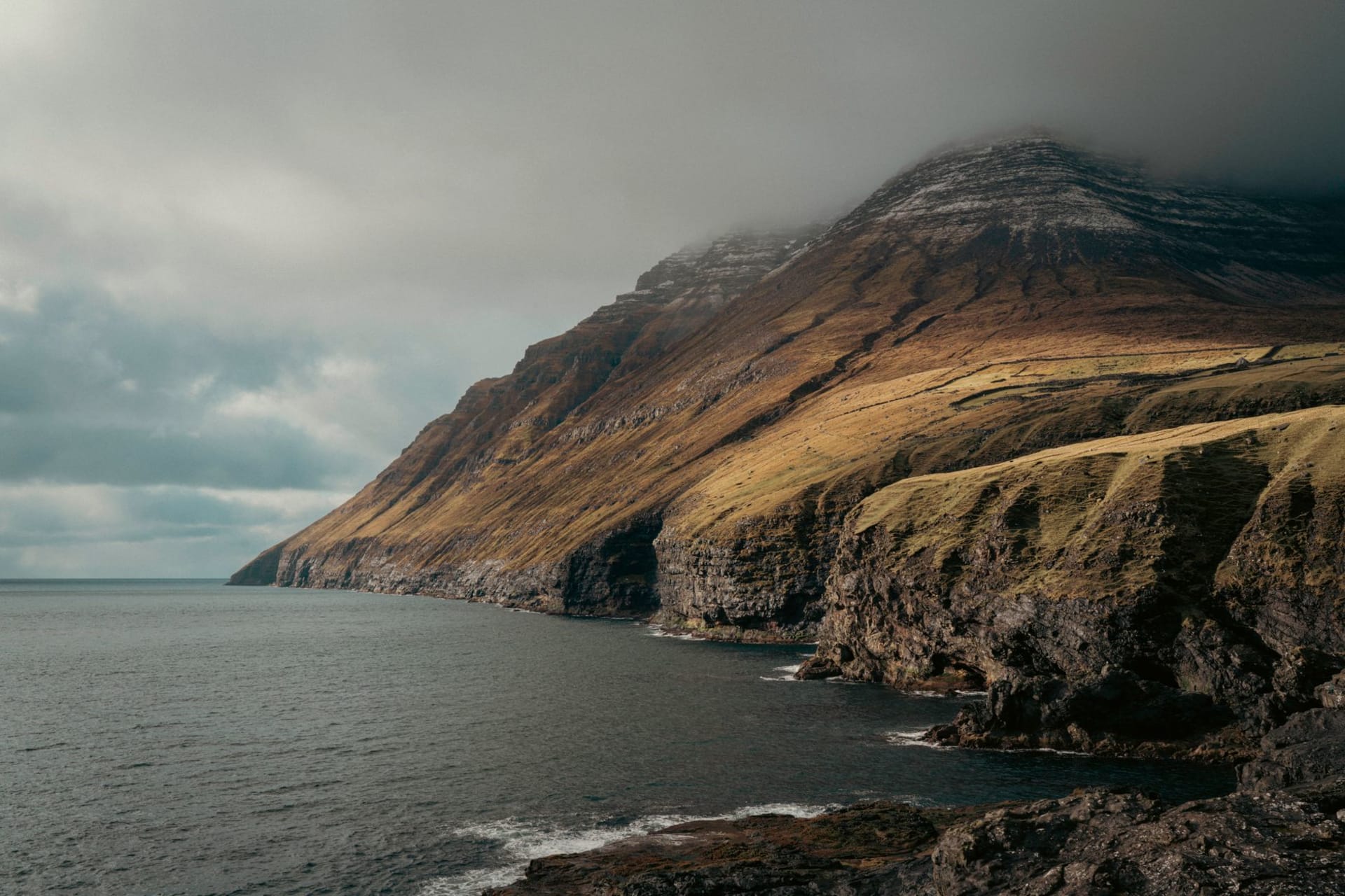 Misty basalt cliffs rising from the North Atlantic on the Faroe Islands, layered in cloud and fog under a grey sky