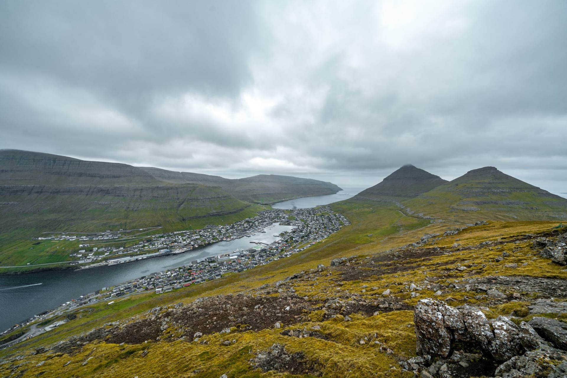 Las paredes de arenisca roja sin techo de la Catedral de Magnus en Kirkjubøur enmarcando un cielo gris pálido, con el sonido de Skopunarfjørður visible más allá