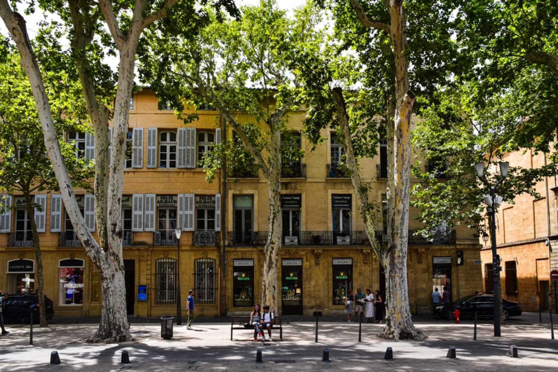 Sun-dappled plane trees lining the Cours Mirabeau in Aix-en-Provence with a stone fountain in the foreground