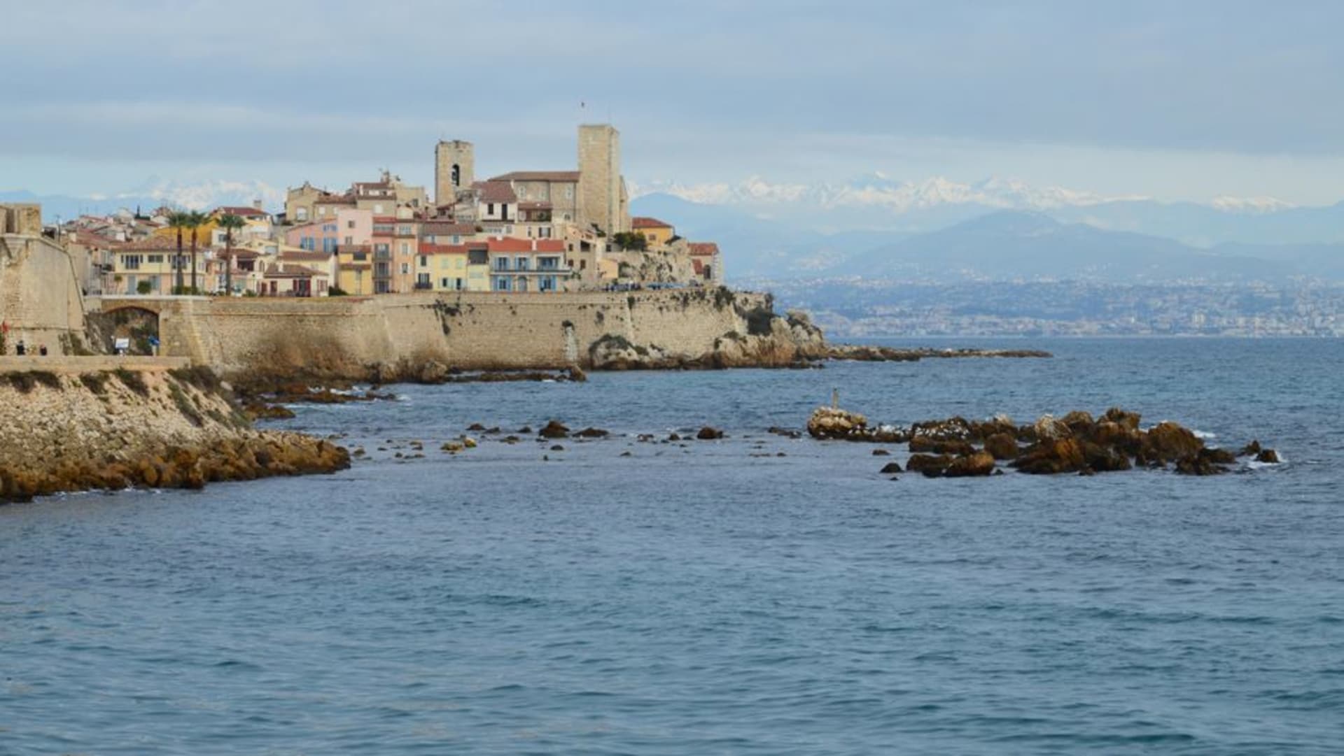 The stone ramparts of Antibes with the old town and sailboats in the harbour below, the Alps visible in the distance