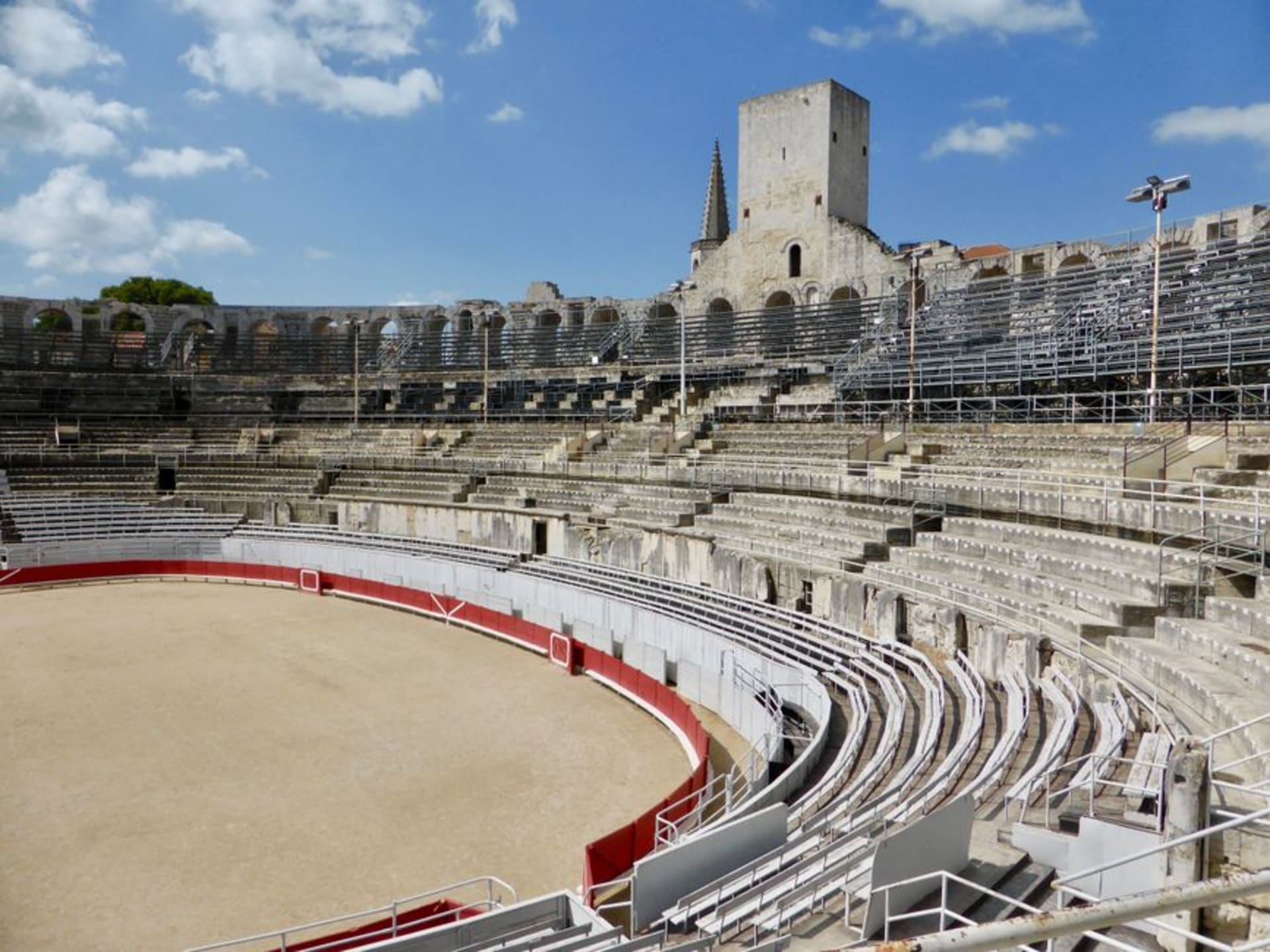 The two-tiered stone arches of the Roman amphitheatre in Arles under a bright Provençal sky