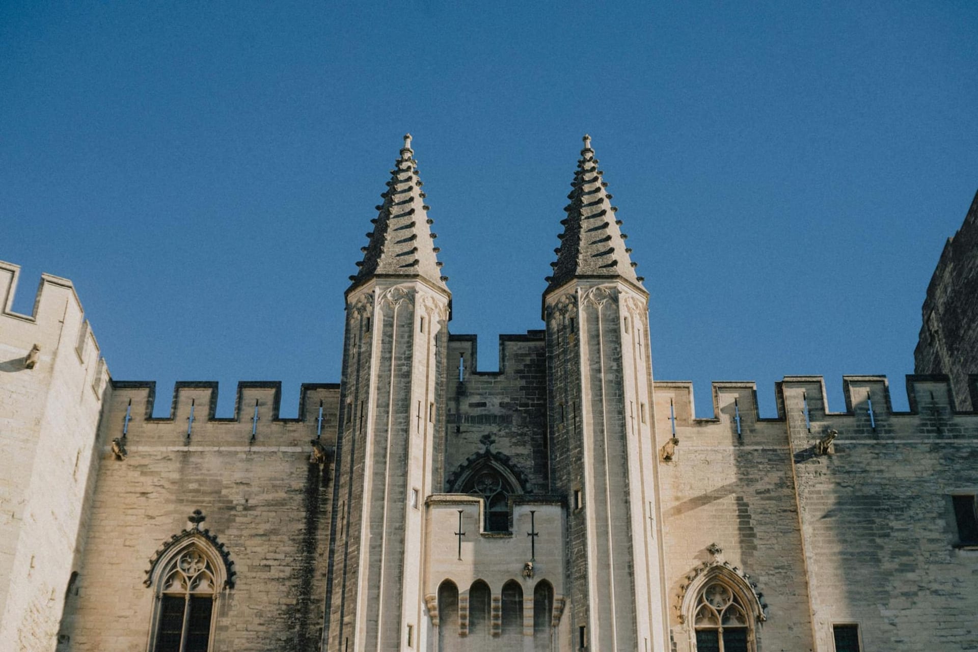 The Palais des Papes rising above Avignon's sun-bleached rooftops, its massive Gothic towers catching the golden light of late afternoon over the Rhône valley