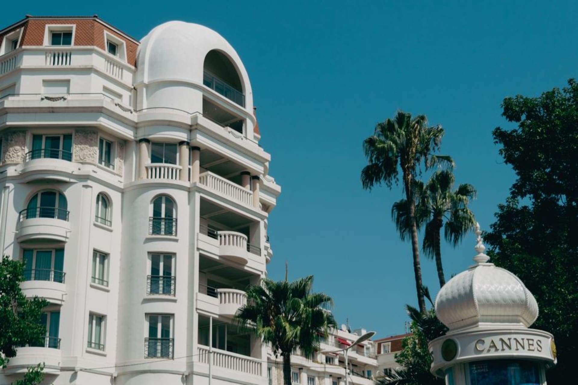 Palm trees and grand hotel façades lining La Croisette in Cannes with yachts moored in the bay