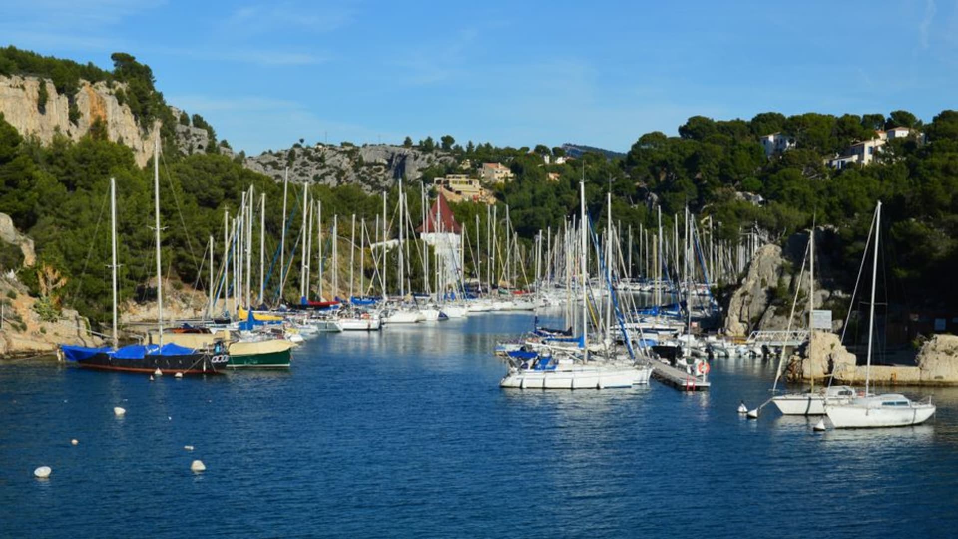 Colourful fishing boats in the small harbour of Cassis with white limestone cliffs rising behind the town