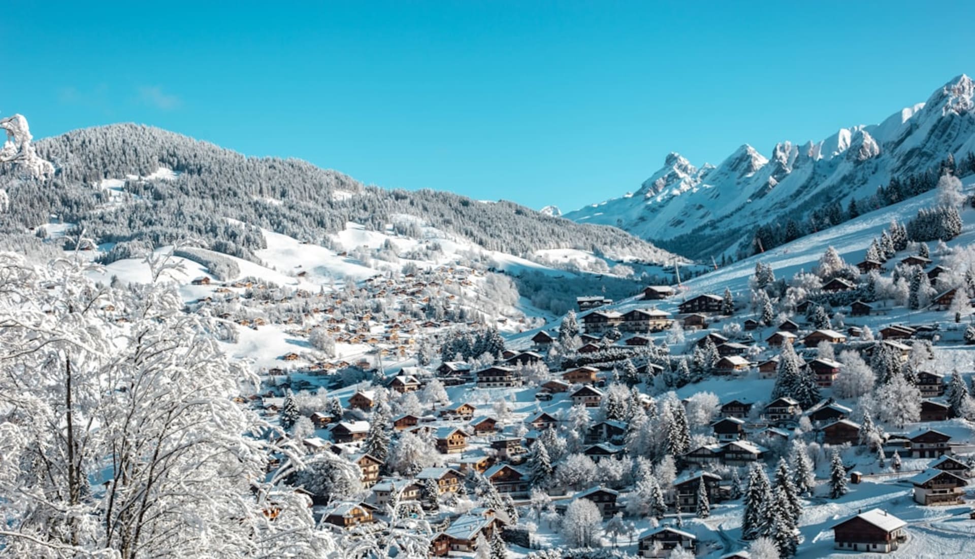 Traditional dark-wood Savoyard chalets with steep snow-covered roofs lining a street in La Clusaz below the Aravis peaks