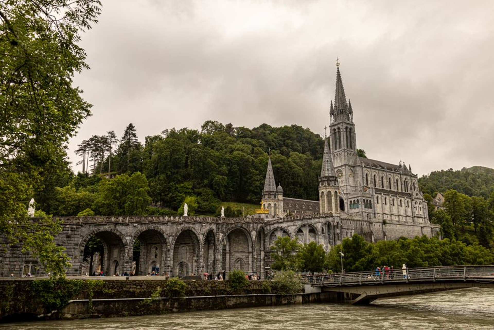 The Sanctuary of Our Lady of Lourdes with its spired basilica lit at dusk against the Pyrenean foothills
