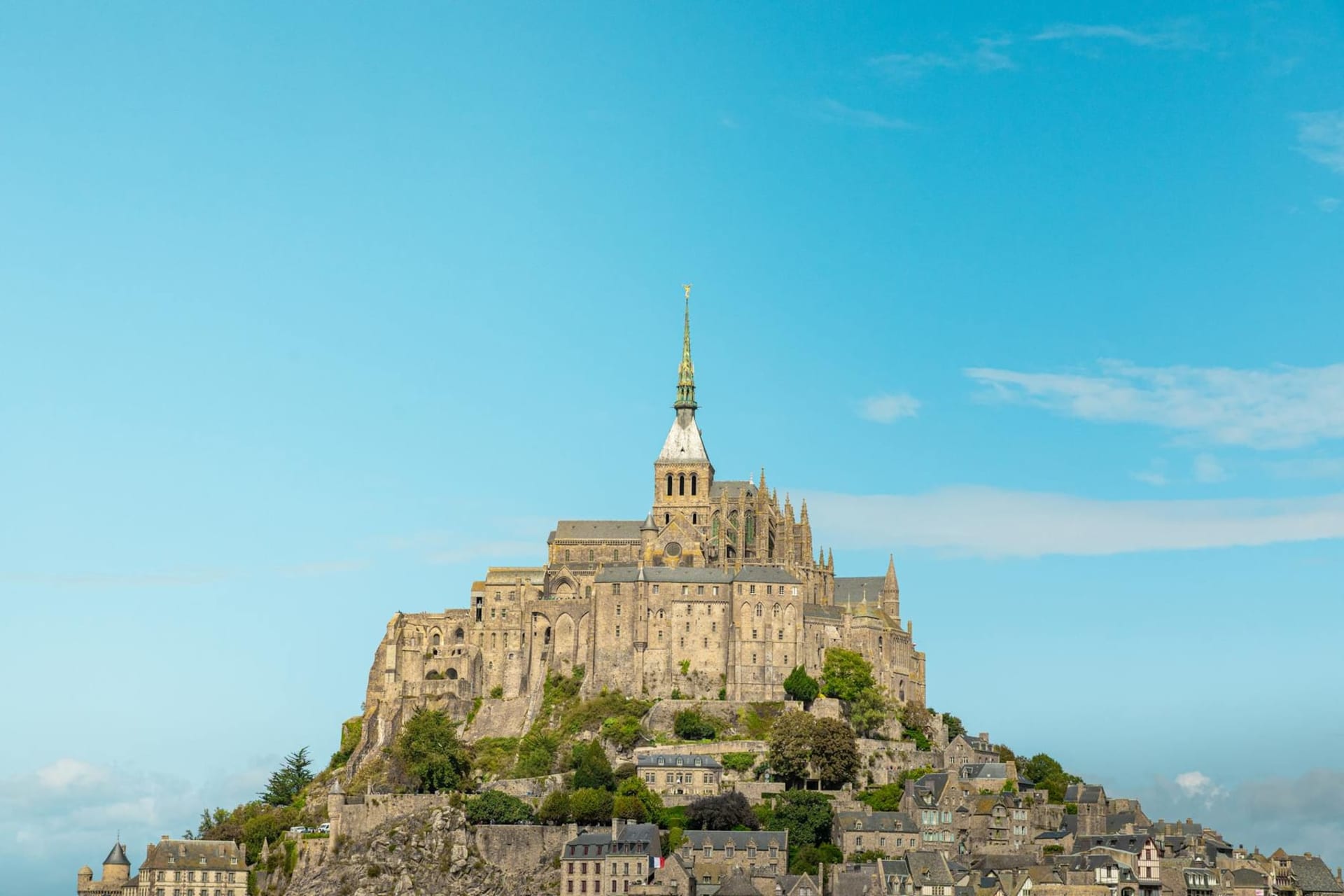 Mont Saint-Michel rising dramatically from the flat Normandy bay at dusk, its Gothic abbey spire piercing a pale sky, the tidal flats reflecting the last light around the island's stone base