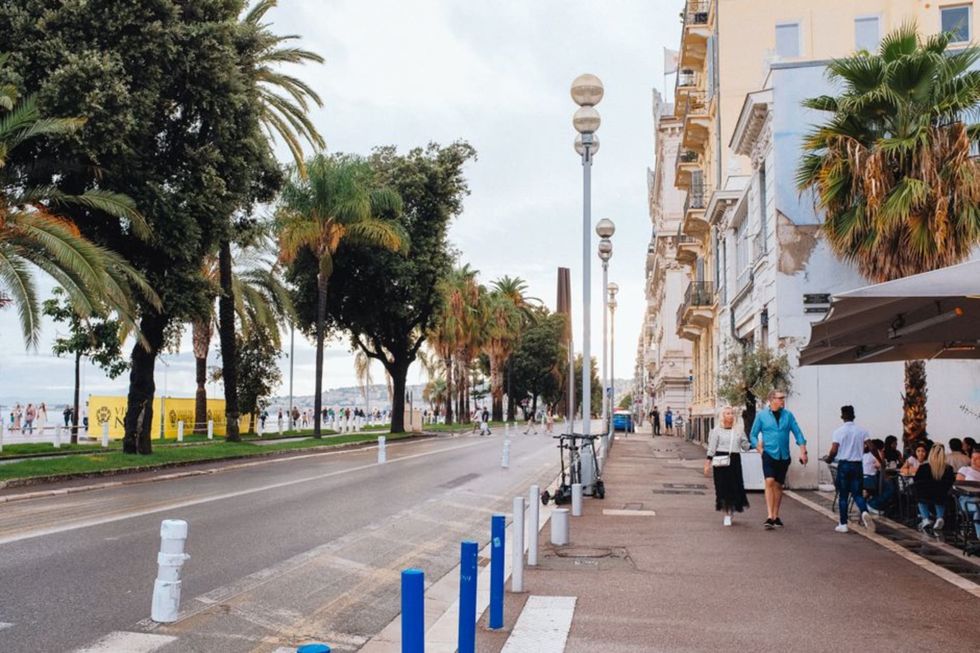 The curving Promenade des Anglais in Nice with palm trees, the pebble beach, and the Baie des Anges beyond