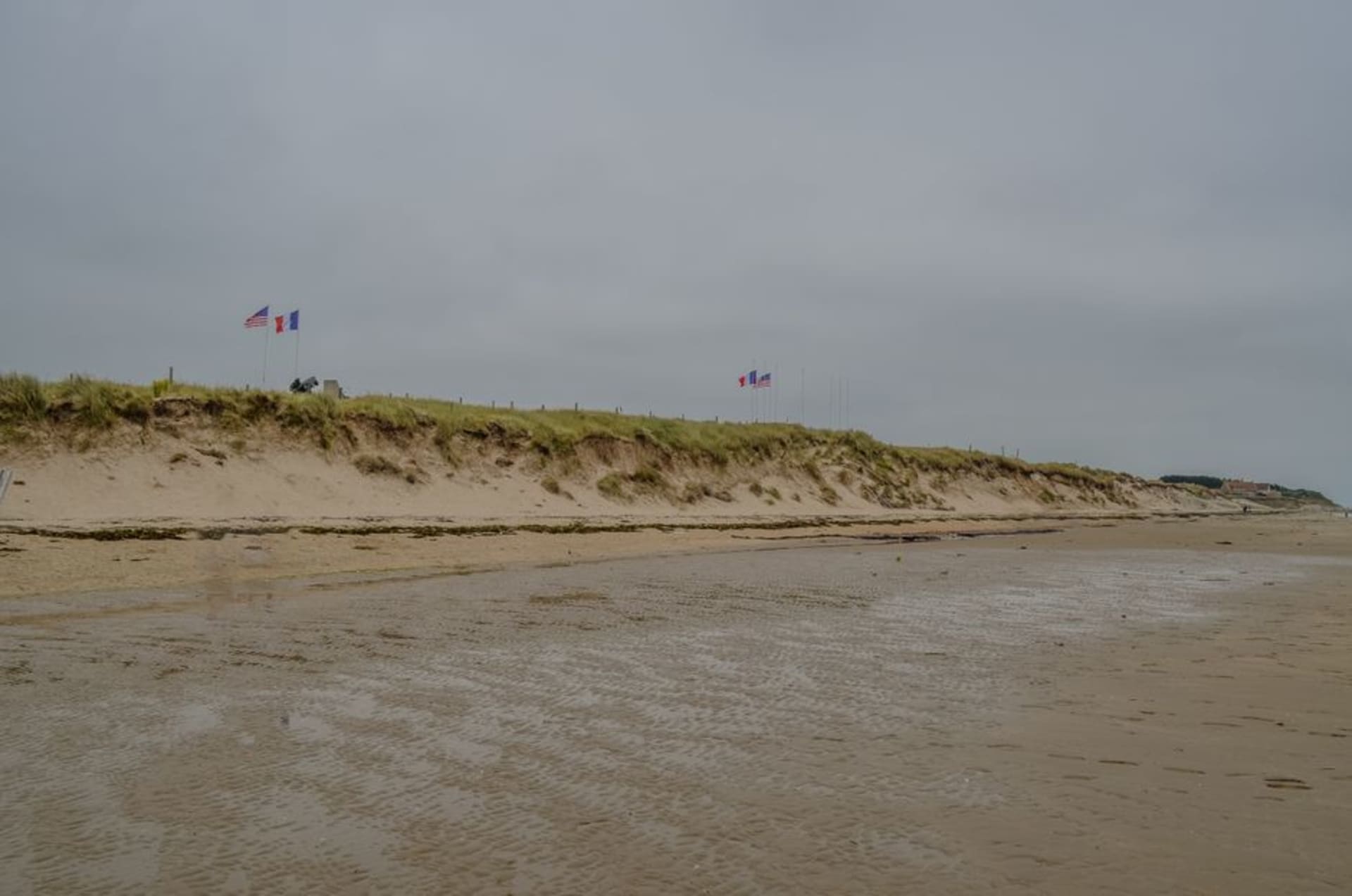 The wide sandy expanse of Omaha Beach at low tide with the bluffs of Colleville-sur-Mer rising behind