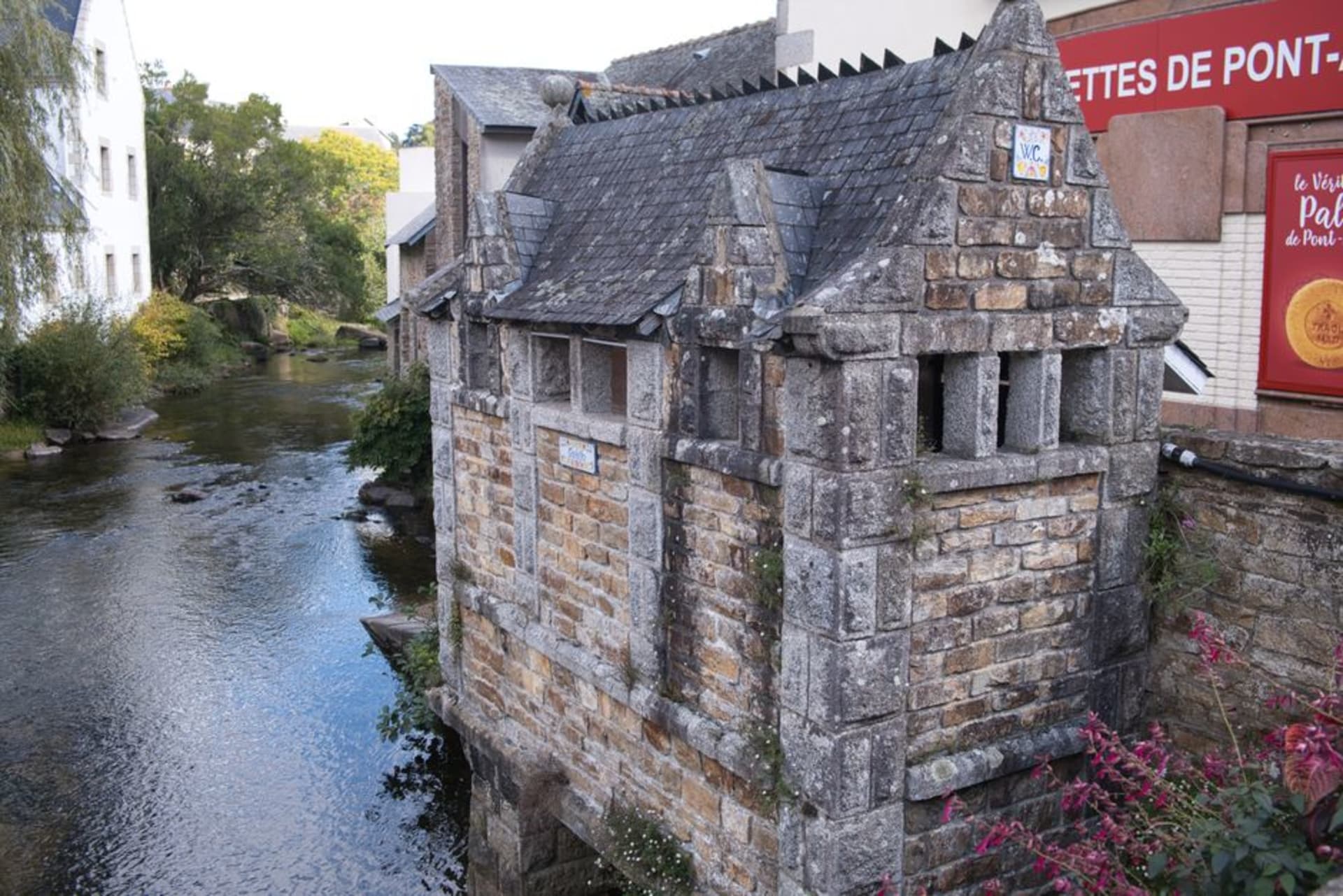 Old stone watermills along the Aven river in Pont-Aven with wooded riverbanks reflected in the water