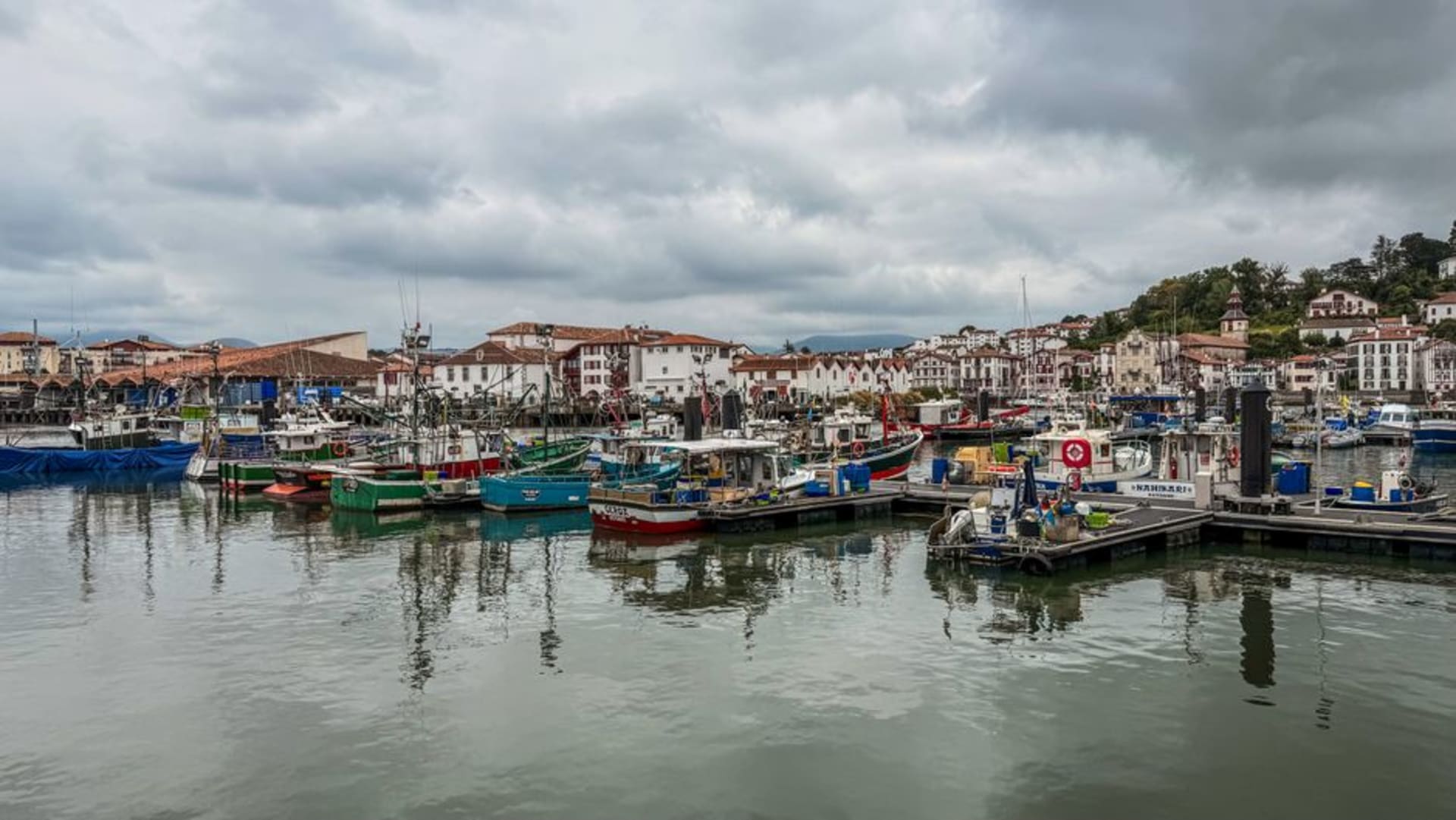 Red and white Basque-style houses lining the curved bay of Saint-Jean-de-Luz with fishing boats moored in the harbour