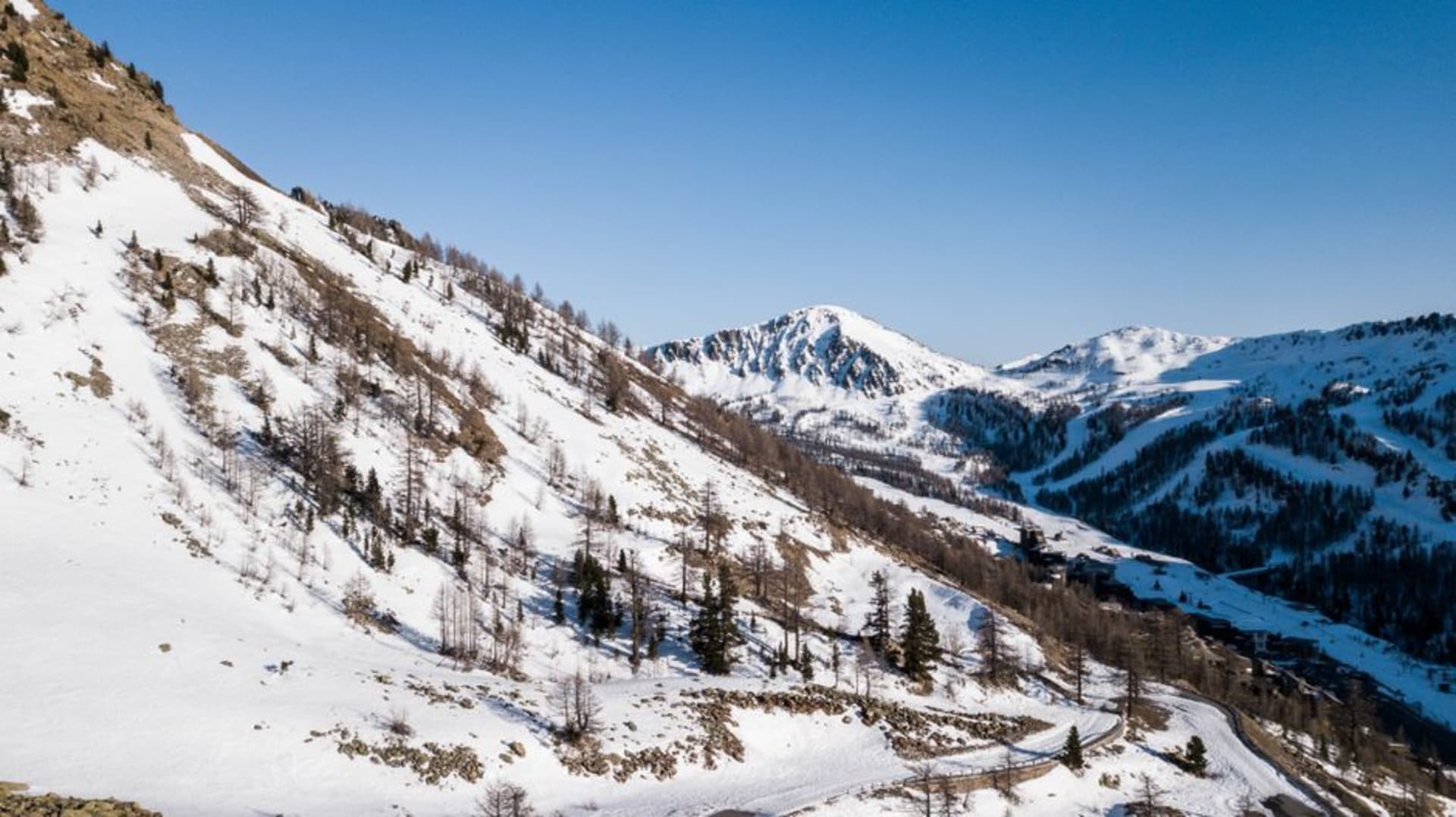 Skiers descending a steep sunlit slope above Val d'Isère with jagged Tarentaise peaks and a clear blue winter sky