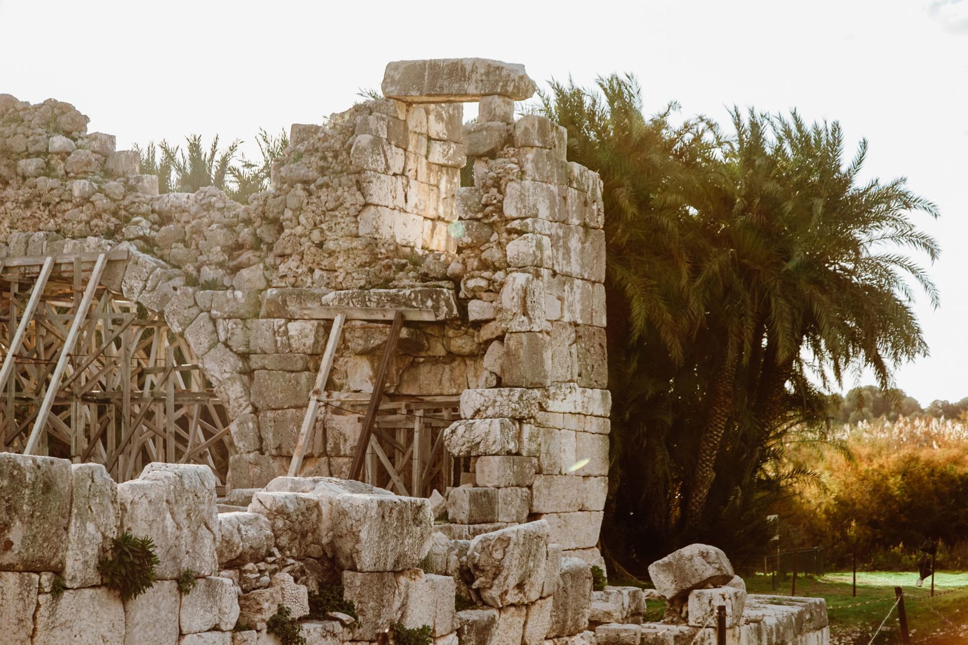 Ancient black basalt ruins of Capernaum with the elevated modern church suspended above on concrete pillars, Sea of Galilee visible behind