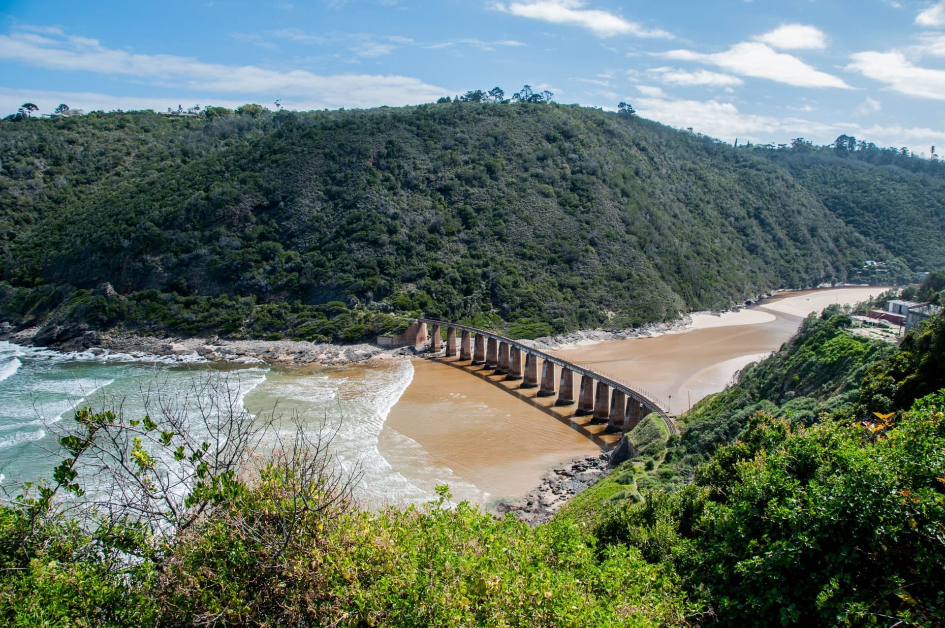 The Knysna railway bridge arching over dense green forest under a wide blue sky