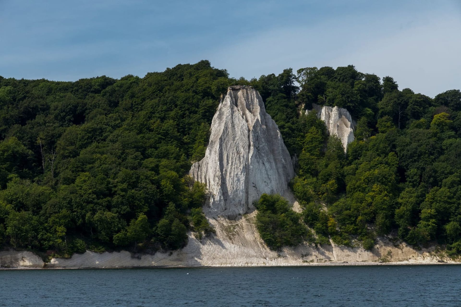 Towering white chalk cliffs of Königsstuhl rising sharply above the deep green Baltic Sea, framed by ancient copper-beech forest in golden afternoon light