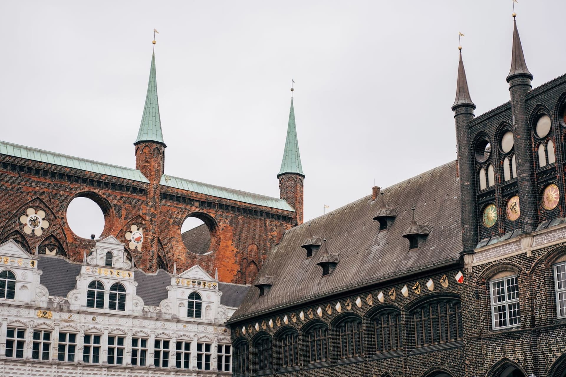 The iconic Holstentor gate rising in red brick against a pale northern sky, its twin towers reflected in the still waters of the Trave River, with the spires of Lübeck's medieval skyline visible behind it