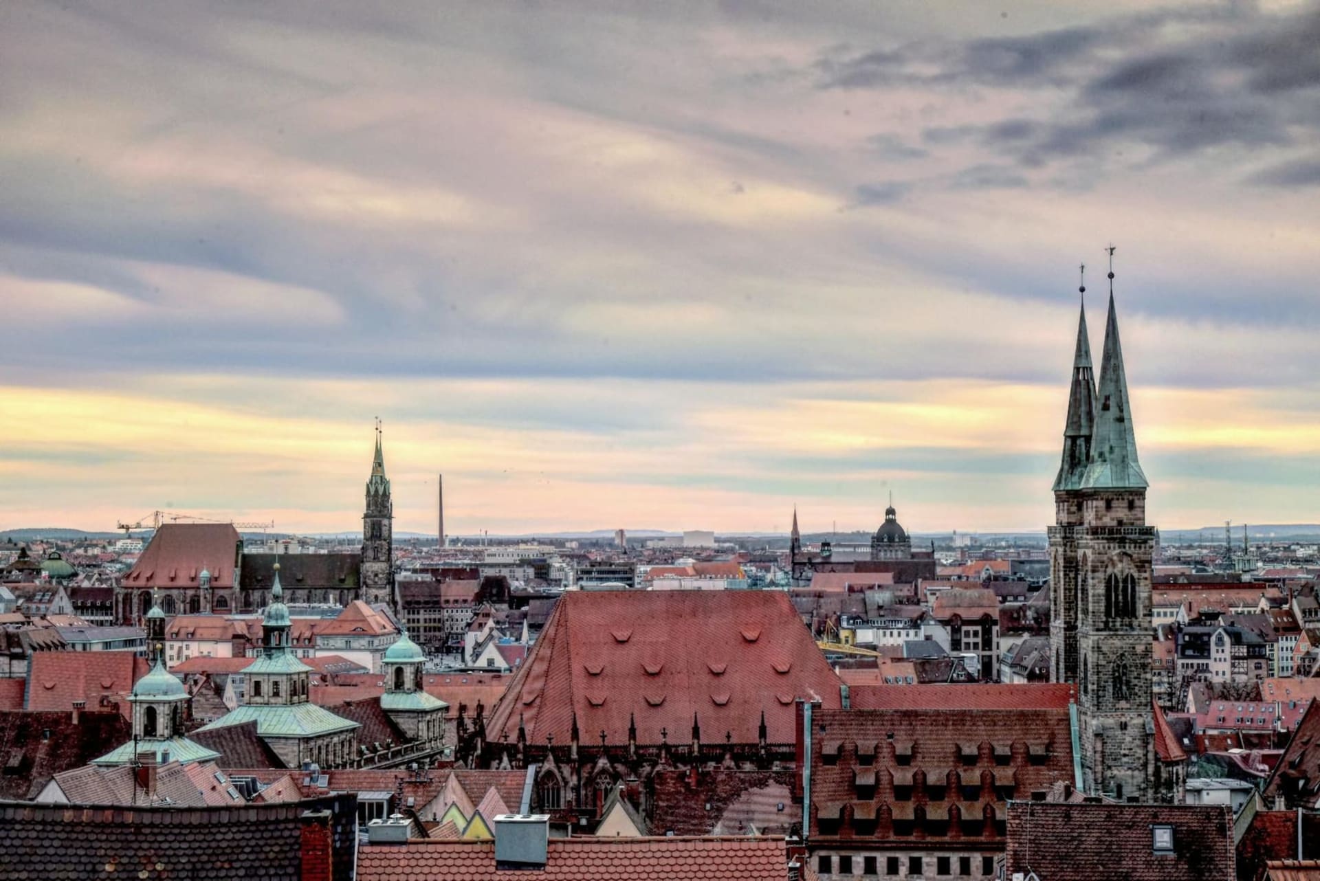The medieval Kaiserburg castle rising above Nuremberg's old town rooftops at golden hour, sandstone towers catching warm amber light against a pale winter sky
